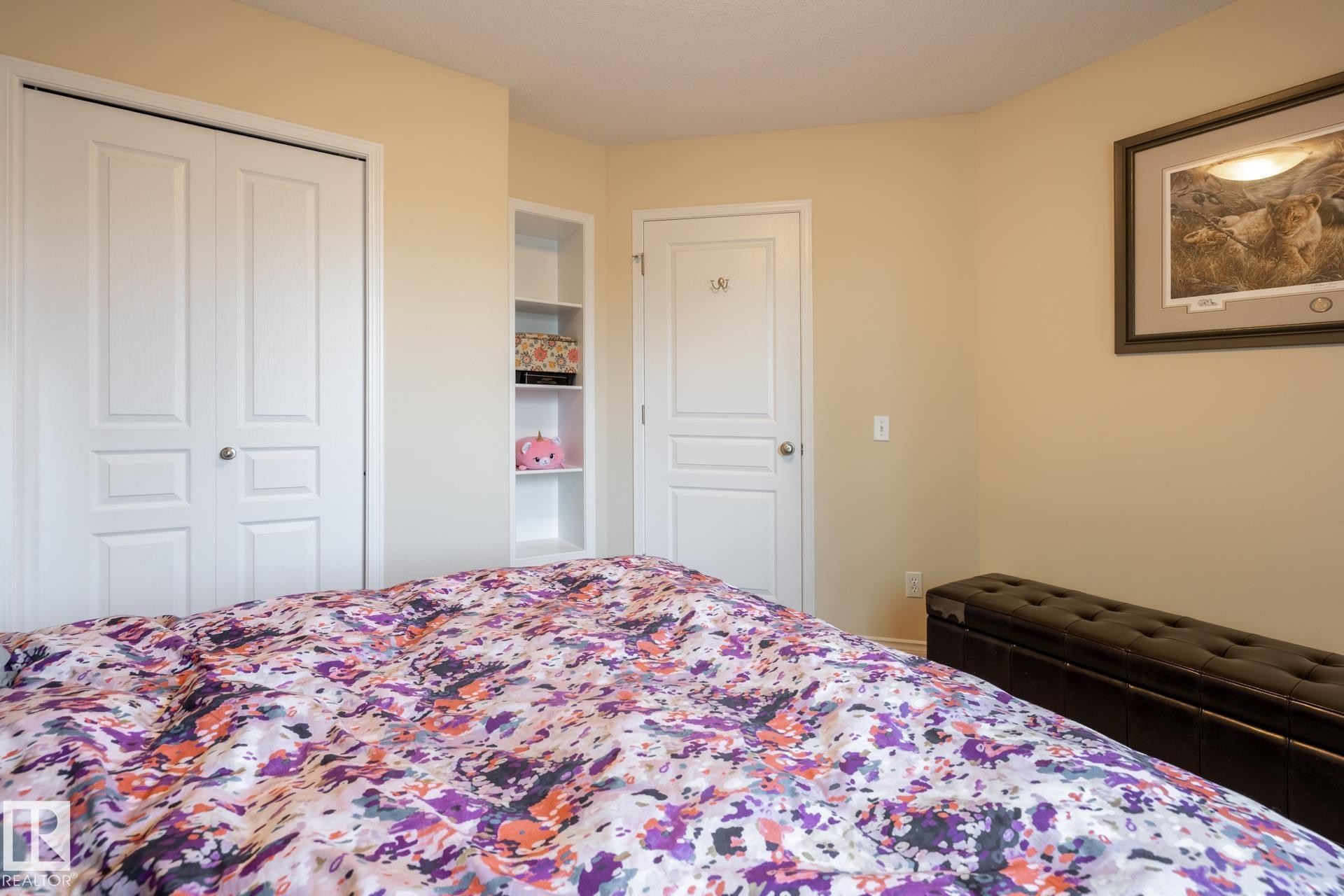 Bedroom featuring a double-door closet, built-in shelving, and a paneled white door with a round knob - 5820 7 Avenue Sw, Edmonton, AB - Indoor Photo Showing Bedroom