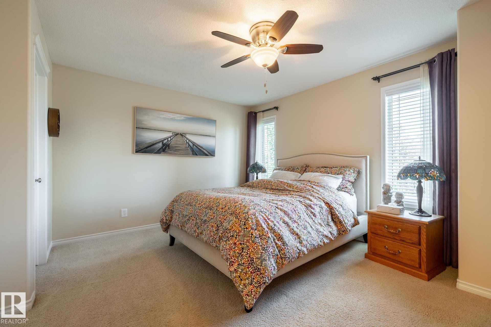 Neutral-toned bedroom featuring wall-to-wall carpeting, two windows with blinds and curtain rods, and a ceiling fan with integrated lighting - 5820 7 Avenue Sw, Edmonton, AB - Indoor Photo Showing Bedroom