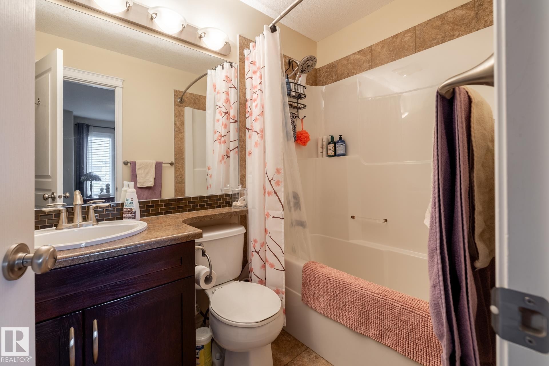 Bathroom featuring a dark wood-finish vanity with a single basin sink, a large mirror, a tiled backsplash, and a combination tub/shower with a tiled surround - 5820 7 Avenue Sw, Edmonton, AB - Indoor Photo Showing Bathroom