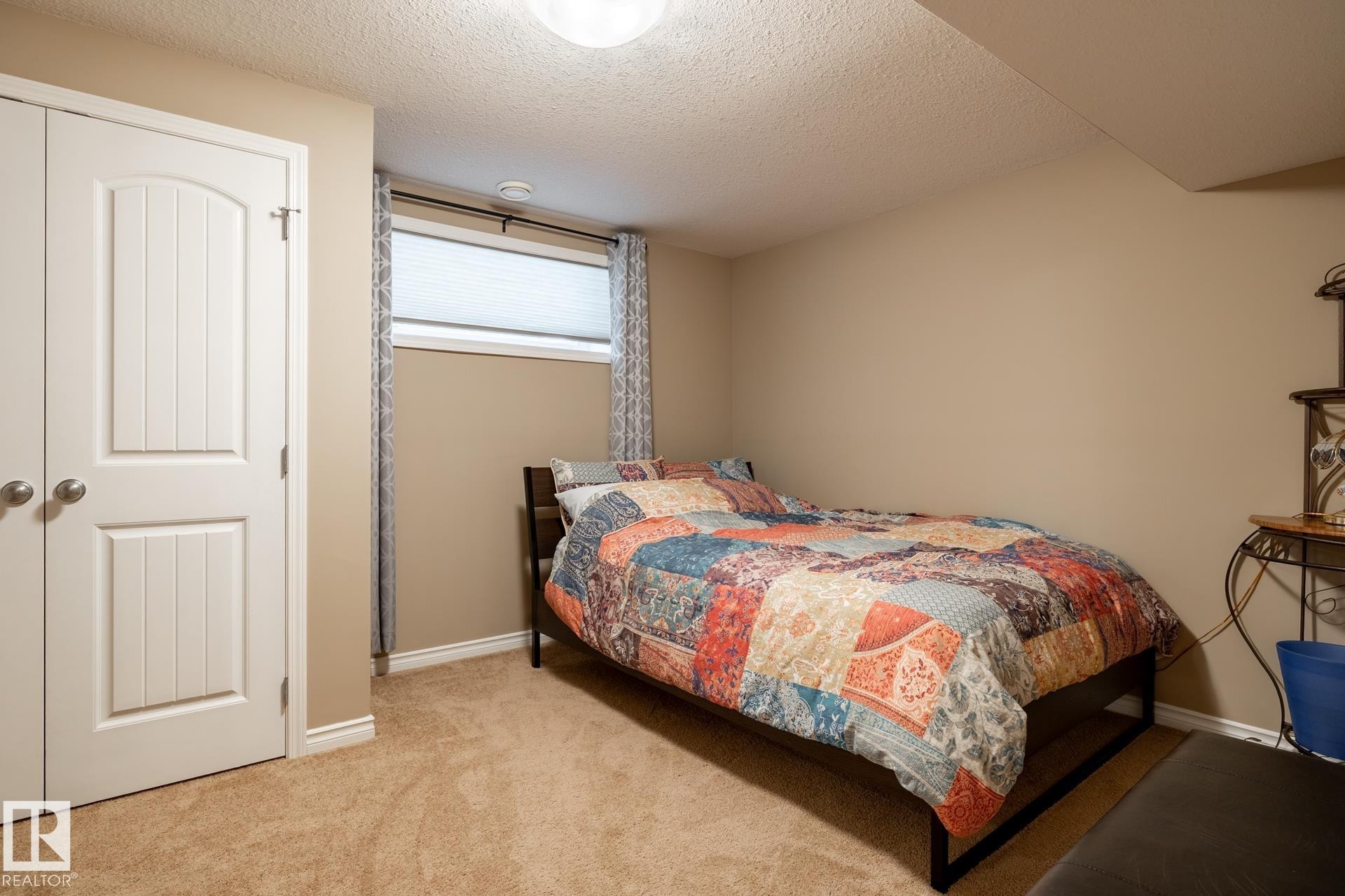 Carpeted bedroom with a window, white window blinds, and patterned curtains - 5820 7 Avenue Sw, Edmonton, AB - Indoor Photo Showing Bedroom