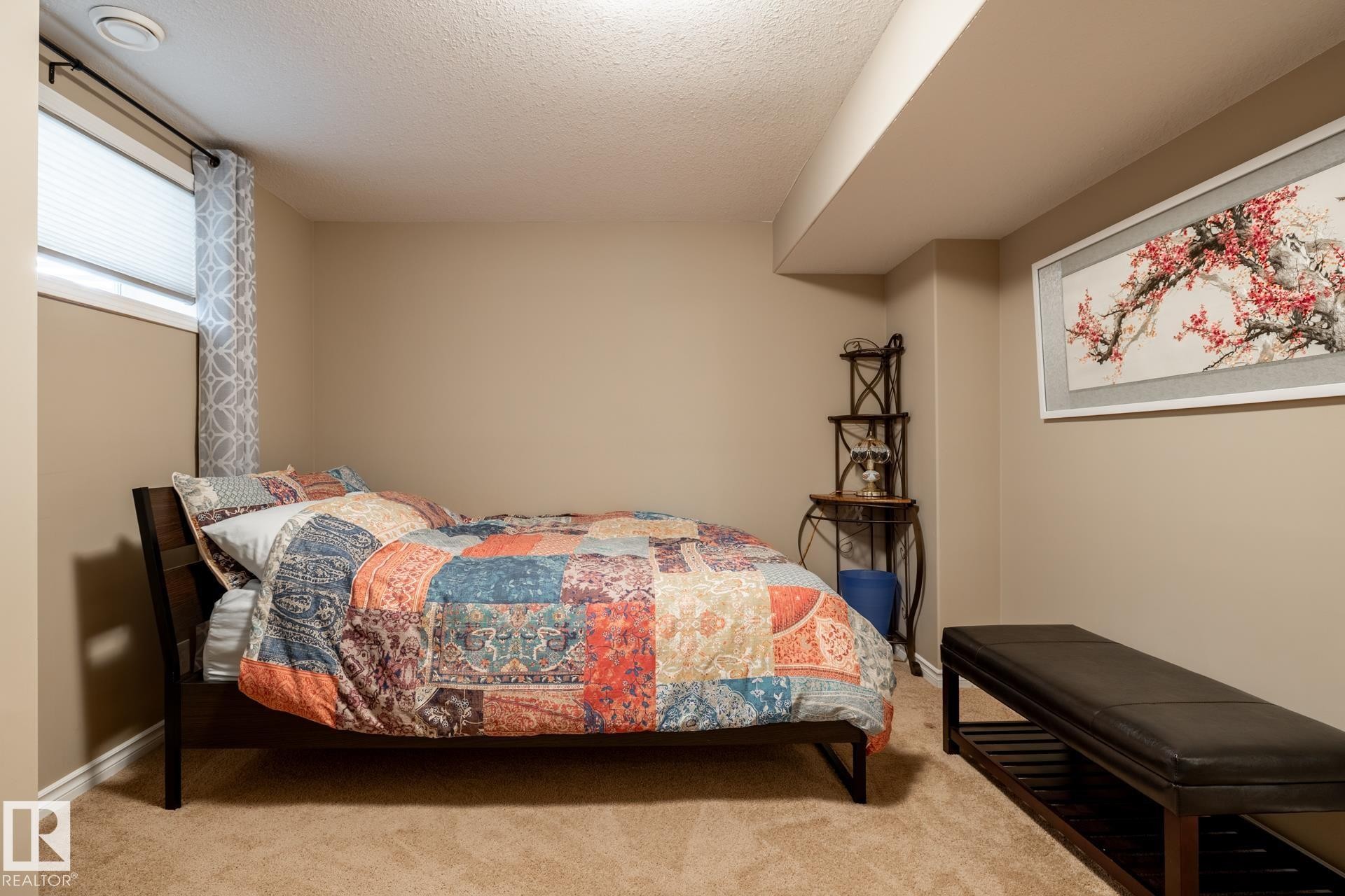 Carpeted interior space featuring a recessed ceiling beam, a rectangular window with horizontal blinds, and neutral wall paint - 5820 7 Avenue Sw, Edmonton, AB - Indoor Photo Showing Bedroom