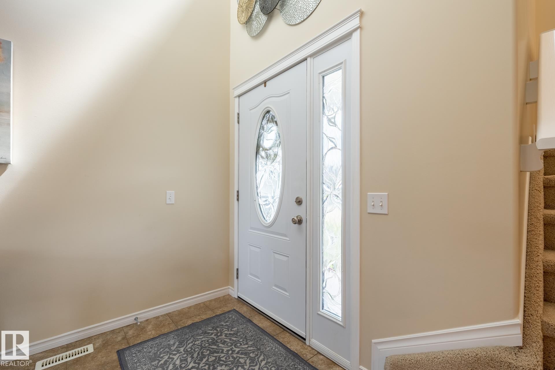 Entryway featuring a white door with an oval-shaped decorative glass insert, a full-length sidelight with patterned glass, tile flooring, and neutral wall tones - 5820 7 Avenue Sw, Edmonton, AB - Indoor Photo Showing Other Room