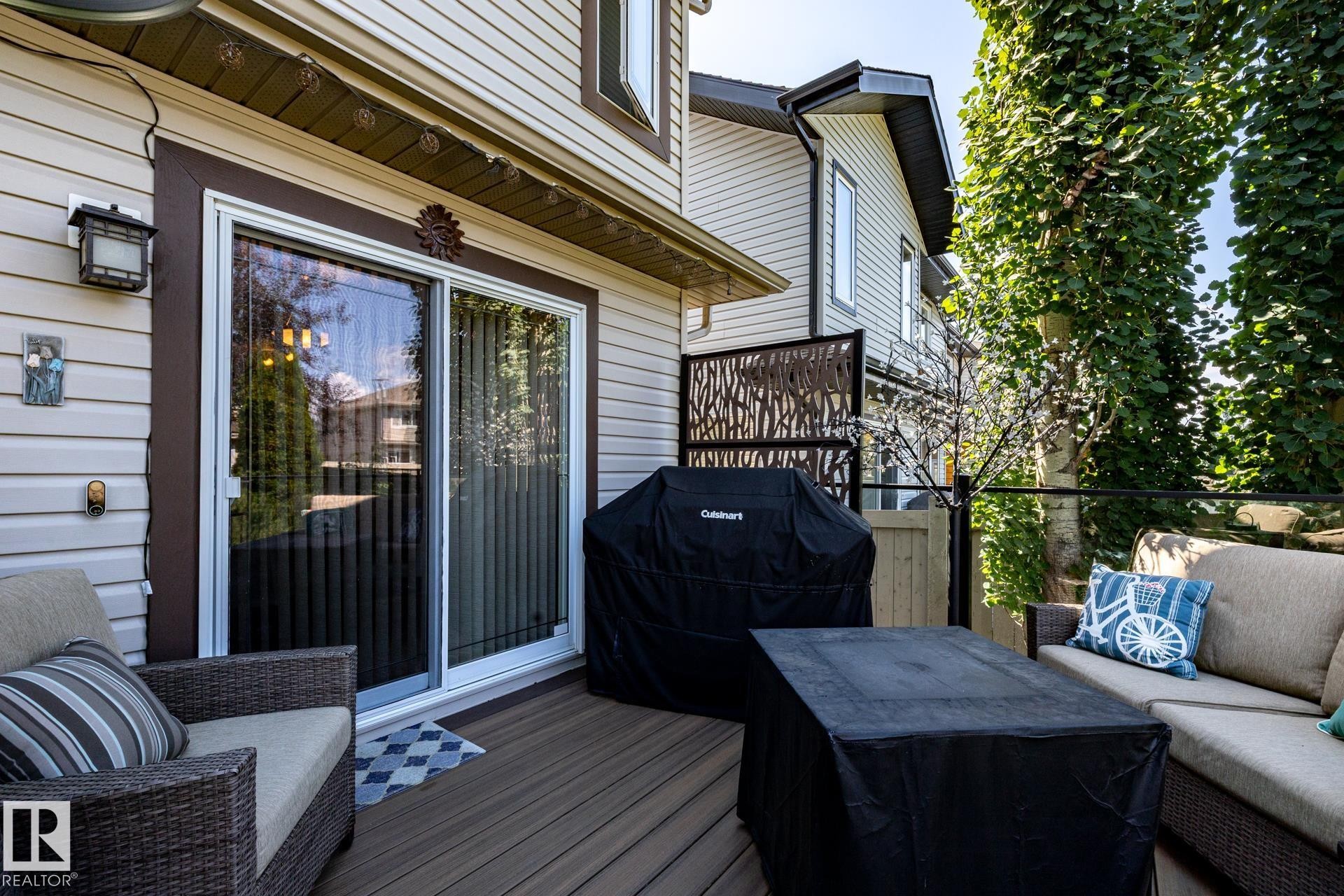 Expansive outdoor deck featuring wood-finish flooring, sliding glass door access, decorative privacy screen, and mature perimeter trees - 5820 7 Avenue Sw, Edmonton, AB - Outdoor With Deck Patio Veranda With Exterior