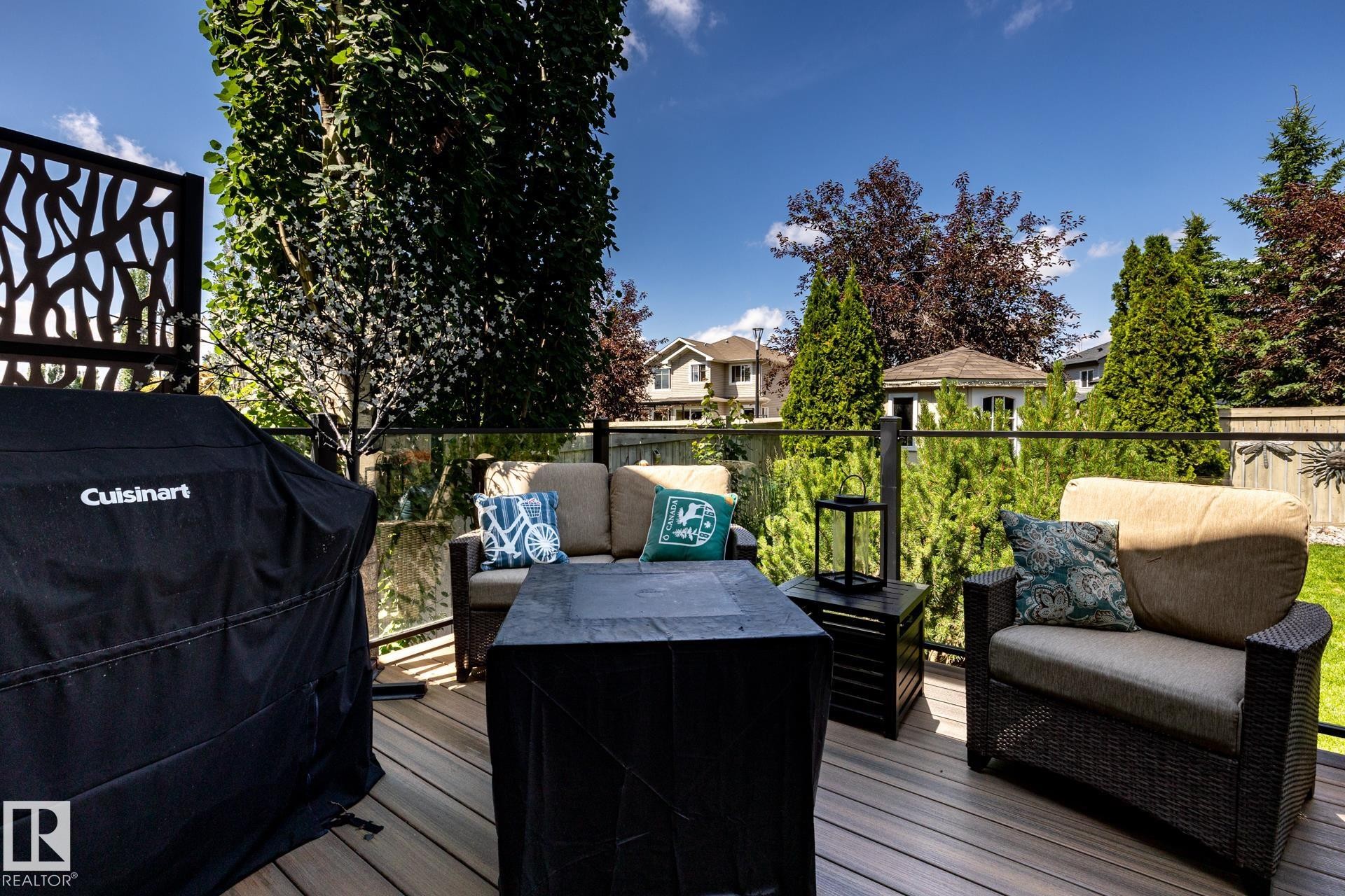 Spacious outdoor deck featuring composite decking, glass panel railings, and a decorative privacy screen - 5820 7 Avenue Sw, Edmonton, AB - Outdoor With Deck Patio Veranda