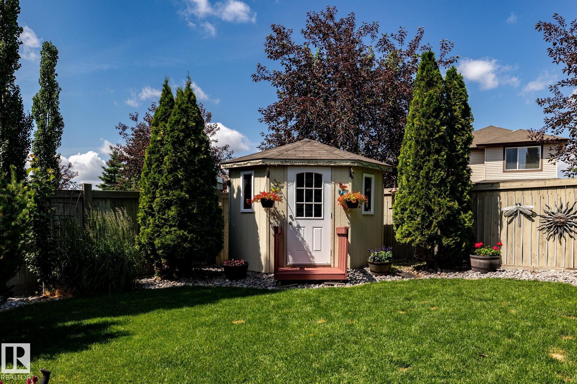 Expansive backyard featuring a manicured lawn and a hexagonal storage shed with a shingled roof, white door, and red-painted steps - 5820 7 Avenue Sw, Edmonton, AB - Outdoor