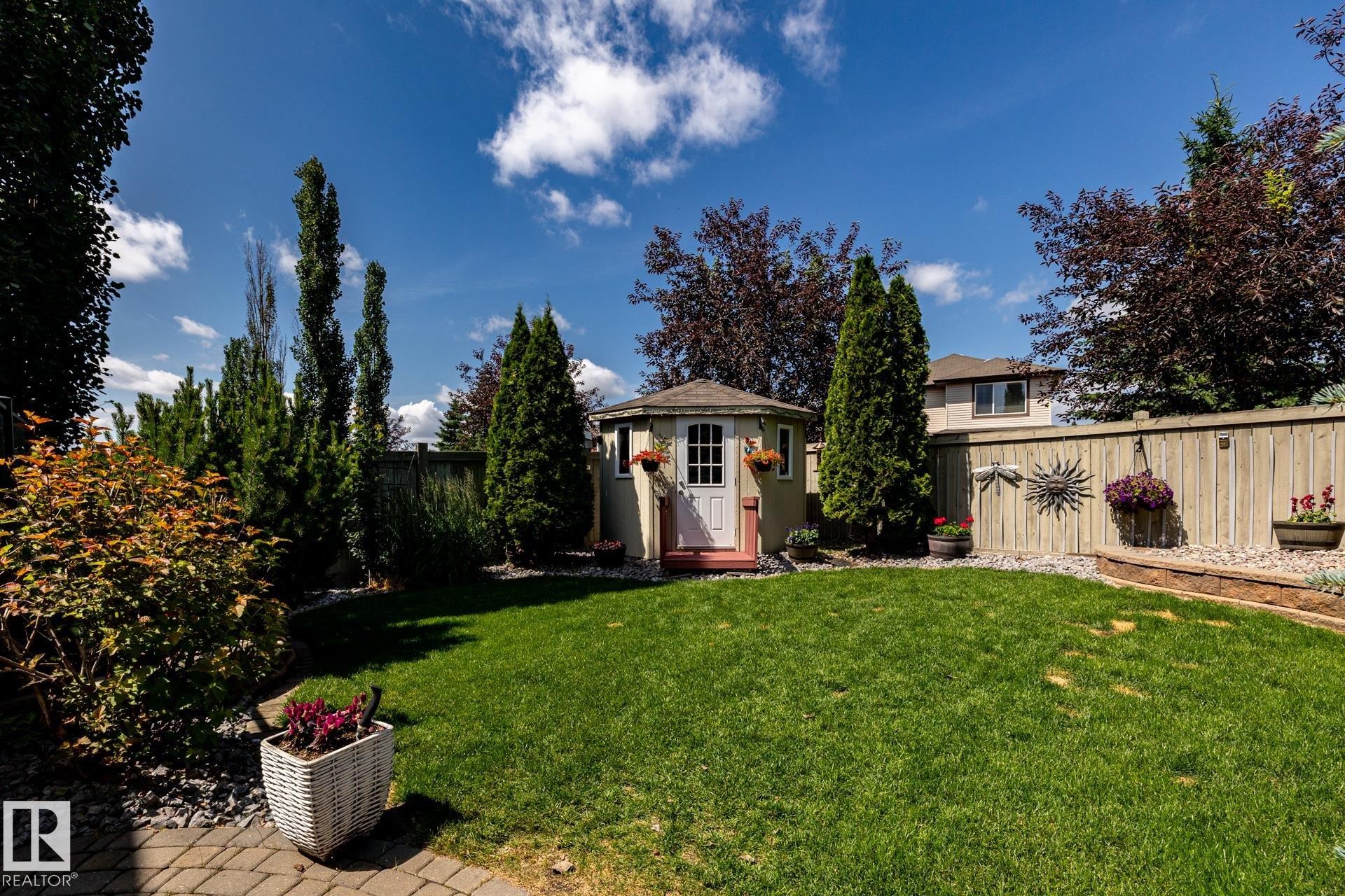 Expansive backyard featuring a central lawn, a garden shed with a white door, a wood privacy fence, and mature trees and shrubs - 5820 7 Avenue Sw, Edmonton, AB - Outdoor