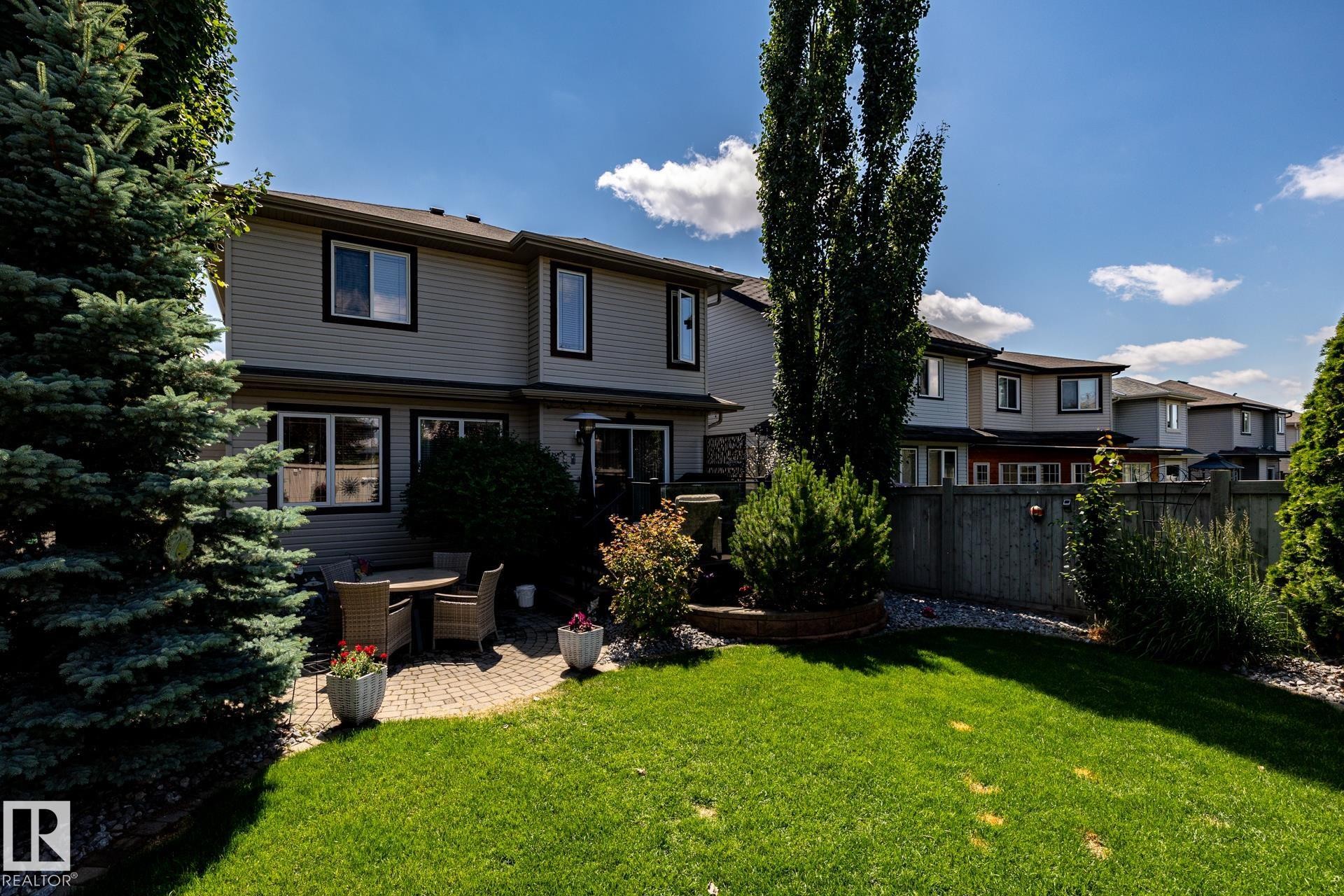 Manicured backyard featuring a paver patio, a lush lawn, mature trees, and privacy fencing - 5820 7 Avenue Sw, Edmonton, AB - Outdoor