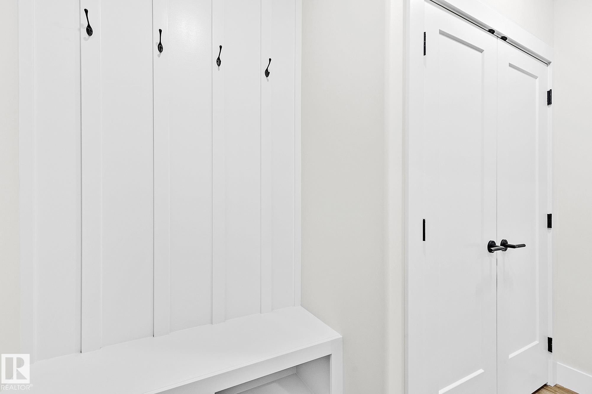 Built-in mudroom bench with vertical paneling and four black coat hooks - 204 Falcon Crescent, Leduc, AB