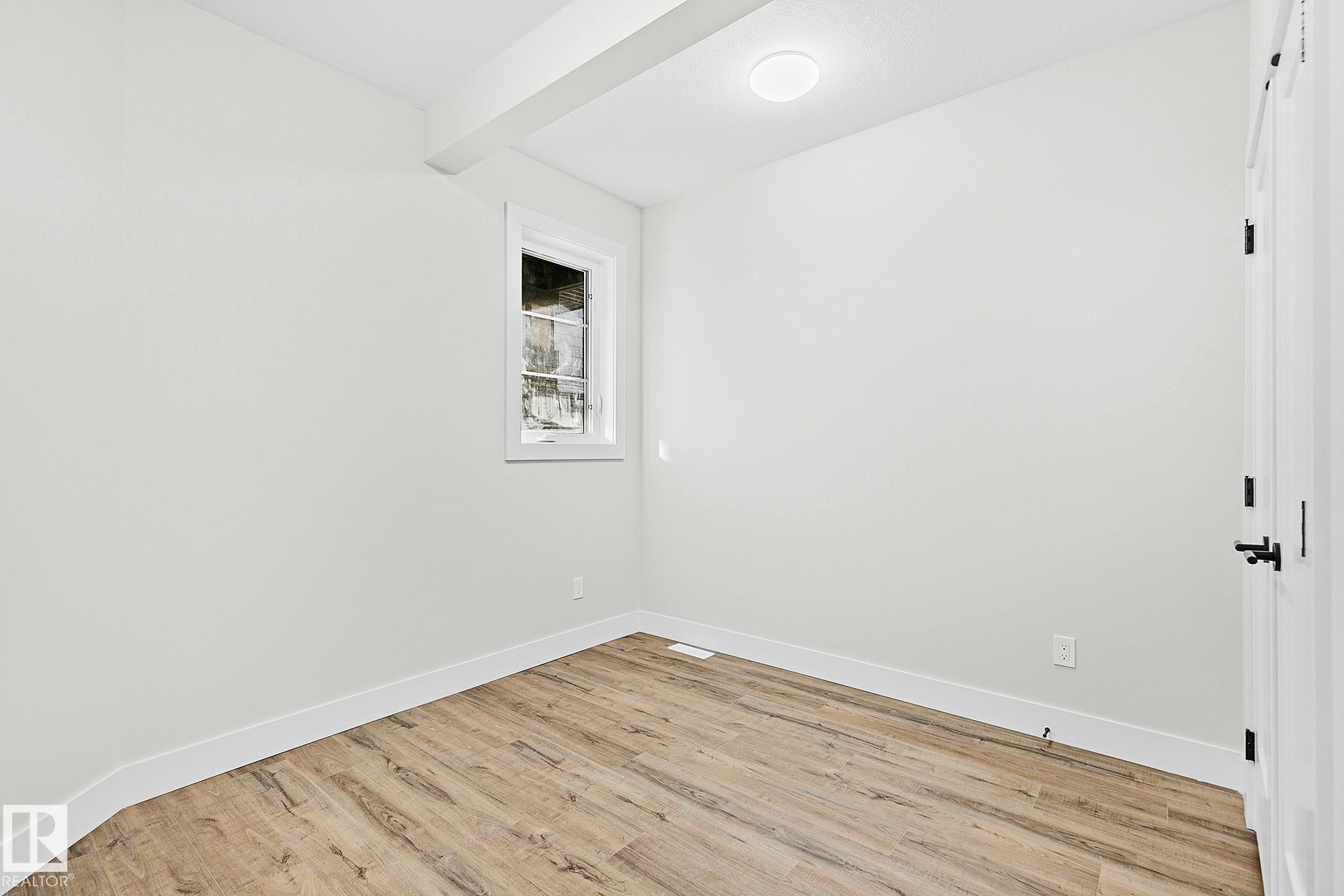 Room featuring wood-finish flooring, white baseboards, and a single window with white trim - 204 Falcon Crescent, Leduc, AB