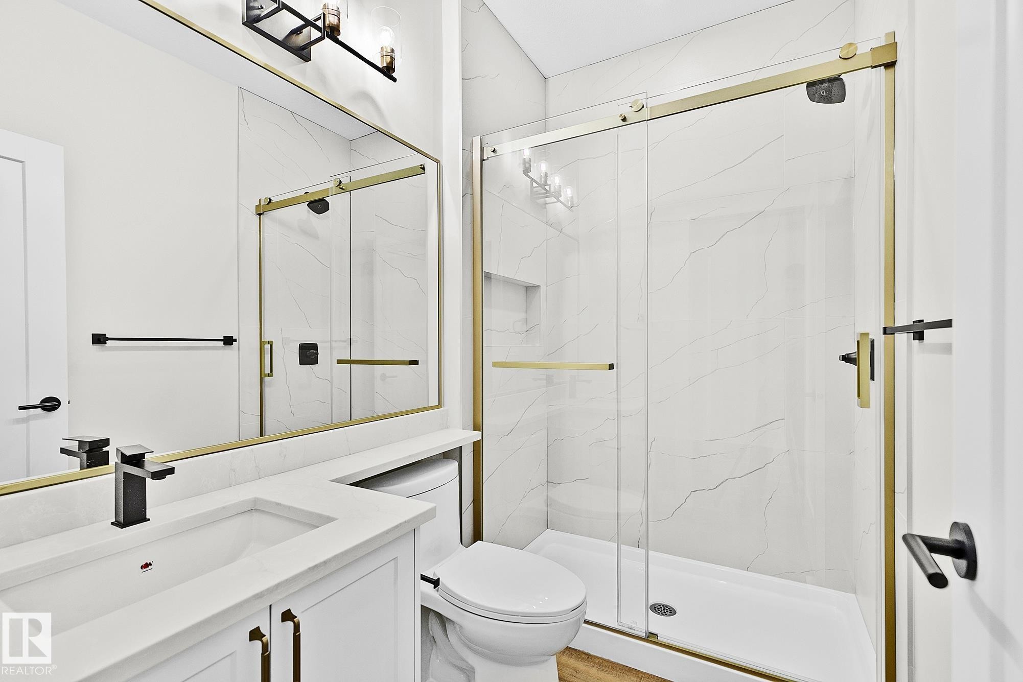 Contemporary bathroom featuring a frameless glass shower with gold-tone hardware, white marble-look shower walls, a built-in shower niche, and a white vanity with a quartz countertop - 204 Falcon Crescent, Leduc, AB