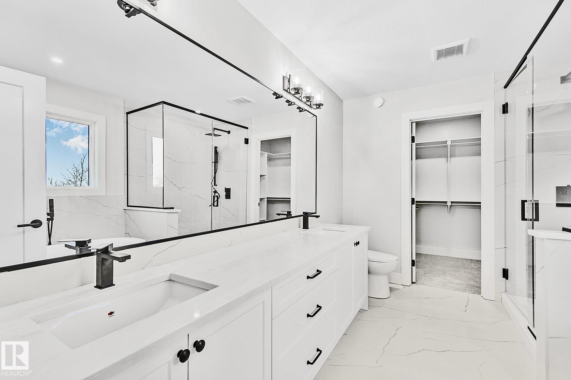 Spacious bathroom with a dual vanity featuring stone countertops and integrated sinks - 204 Falcon Crescent, Leduc, AB