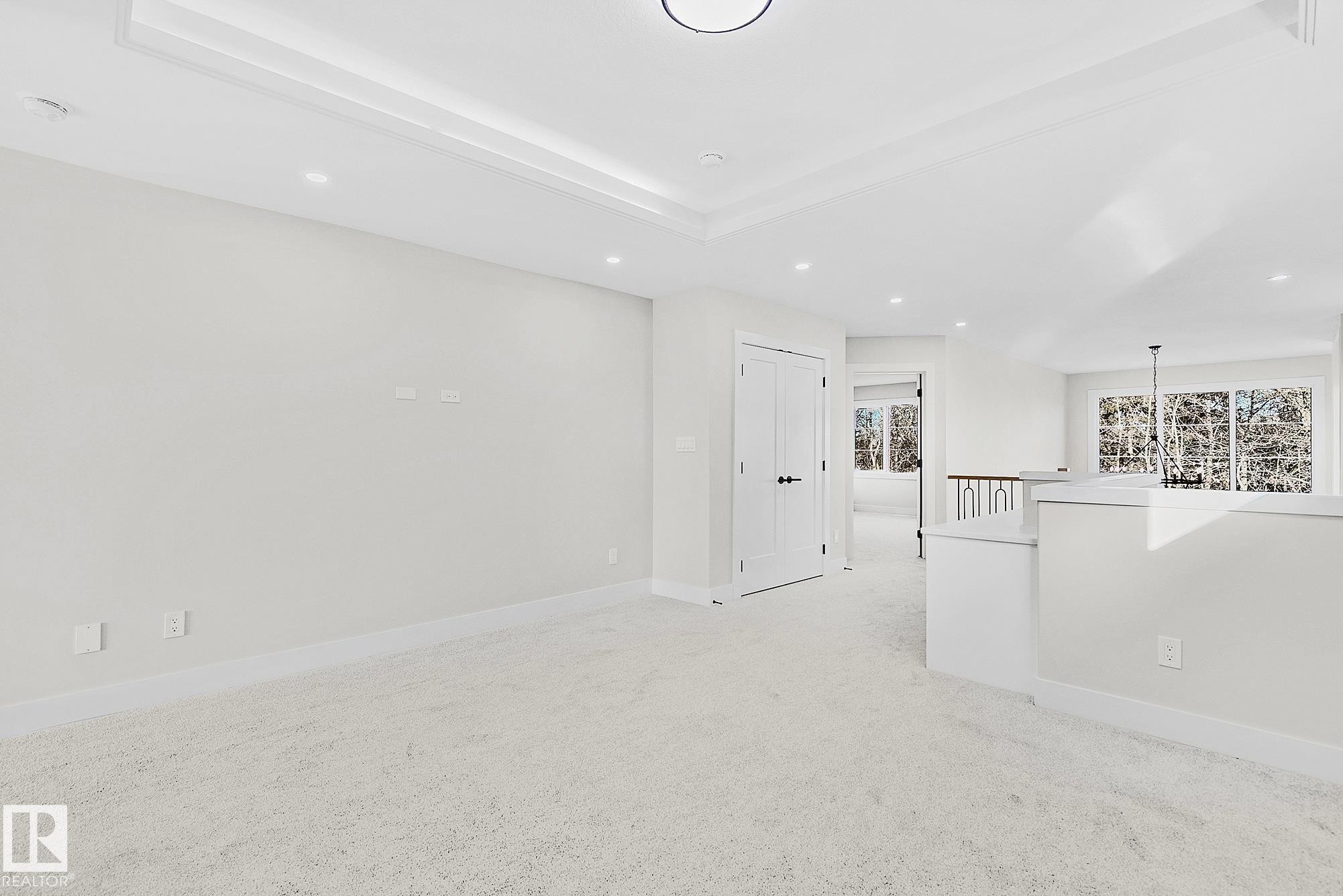 Spacious interior room featuring light-toned carpeting and a tray ceiling with recessed lighting - 204 Falcon Crescent, Leduc, AB