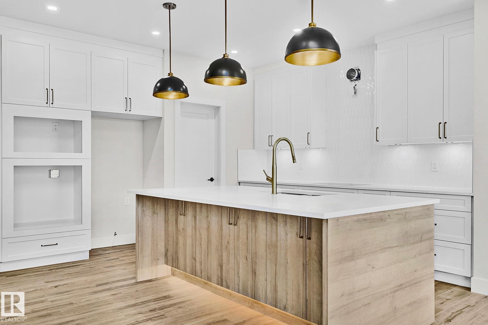Modern kitchen island with wood-finish paneling, white countertop, and integrated sink with a brass-finish gooseneck faucet - 204 Falcon Crescent, Leduc, AB