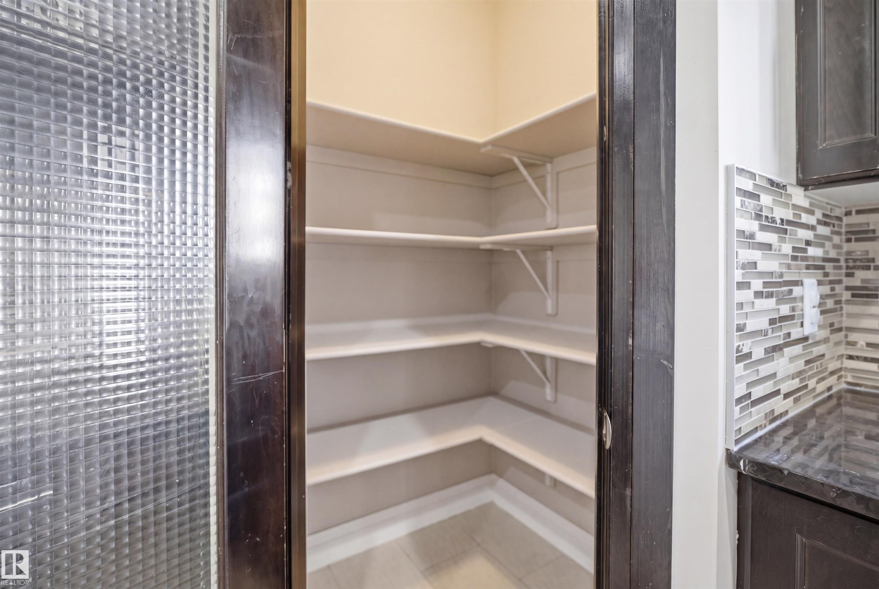 Walk-in pantry featuring corner shelving, light-toned walls, and tile flooring - 16807 54 Street, Edmonton, AB - Indoor With Storage