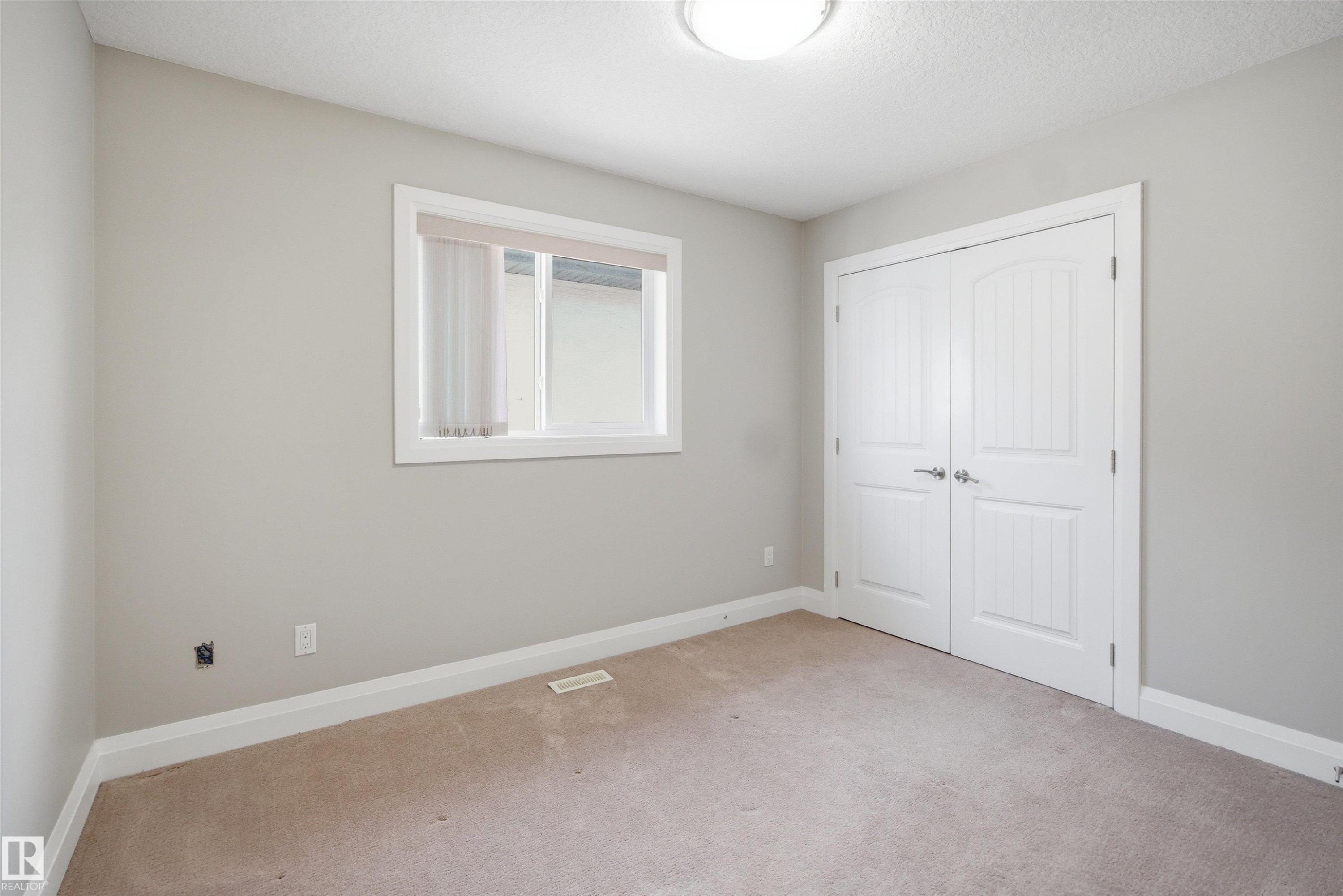 Carpeted room featuring a double-pane window, flush-mount ceiling light, white trim, and a double-door closet with polished chrome hardware - 16807 54 Street, Edmonton, AB - Indoor Photo Showing Other Room