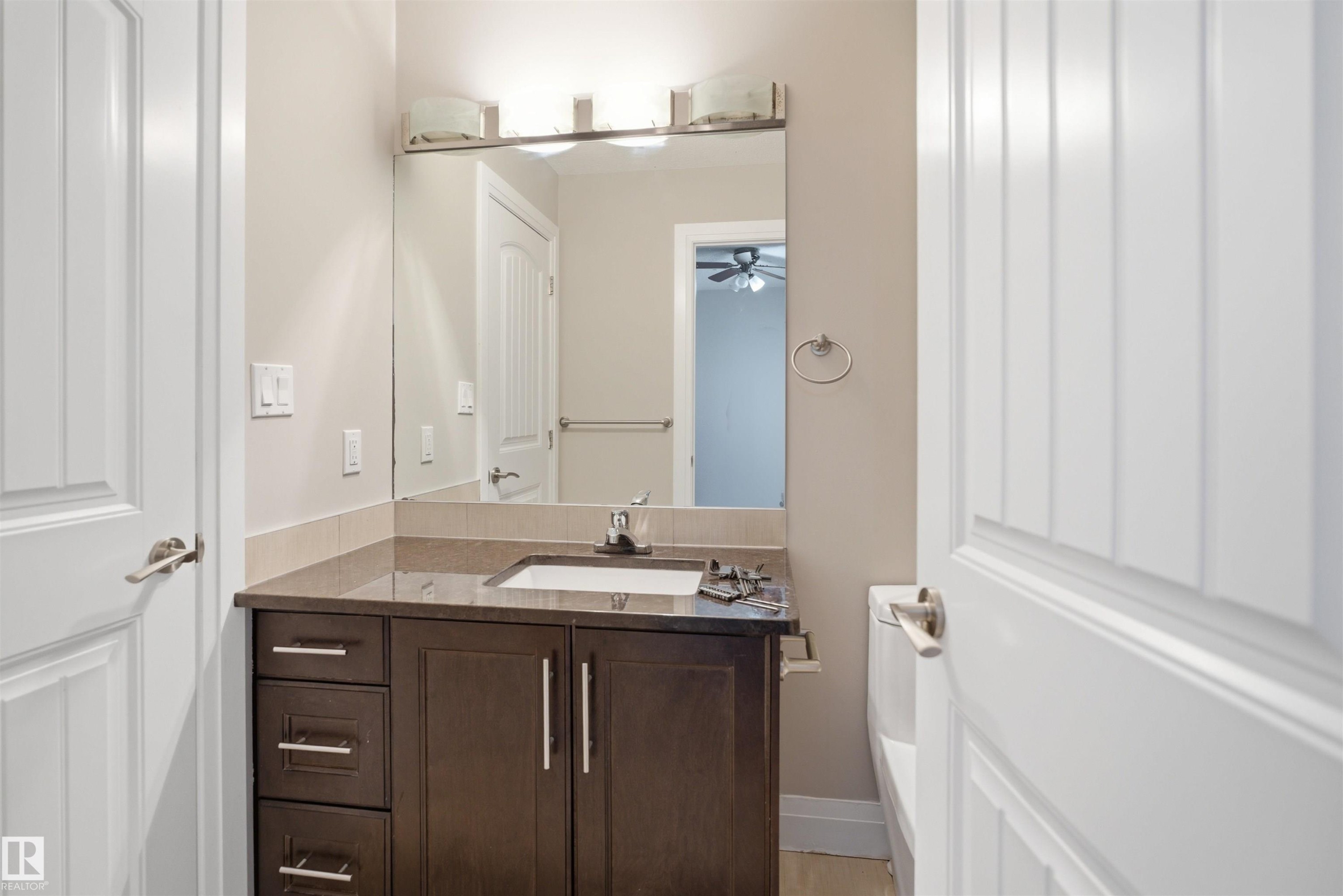 Bathroom vanity featuring a single undermount sink, dark wood cabinetry with brushed nickel hardware, and a stone countertop - 16807 54 Street, Edmonton, AB - Indoor Photo Showing Bathroom