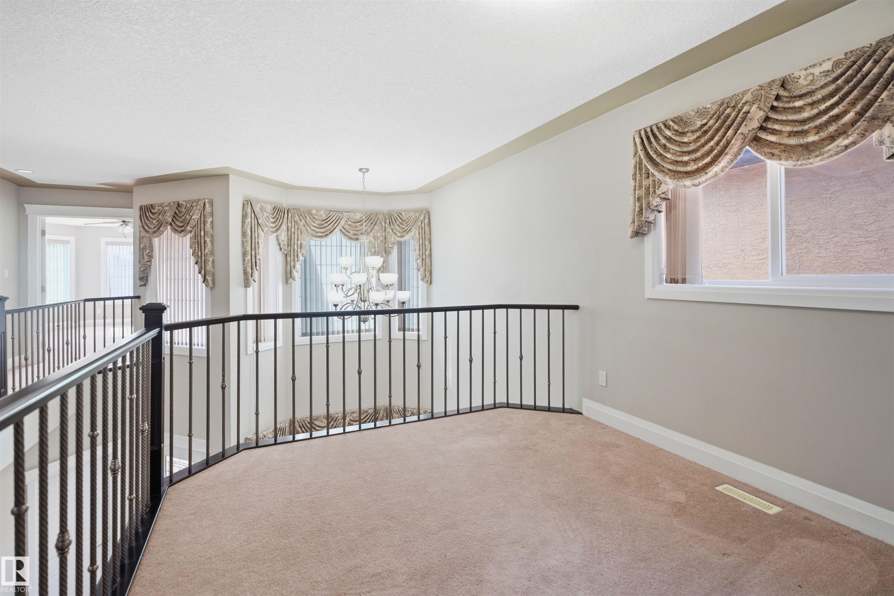 Spacious upper-level landing featuring neutral carpeting and a decorative wrought iron railing - 16807 54 Street, Edmonton, AB - Indoor Photo Showing Other Room