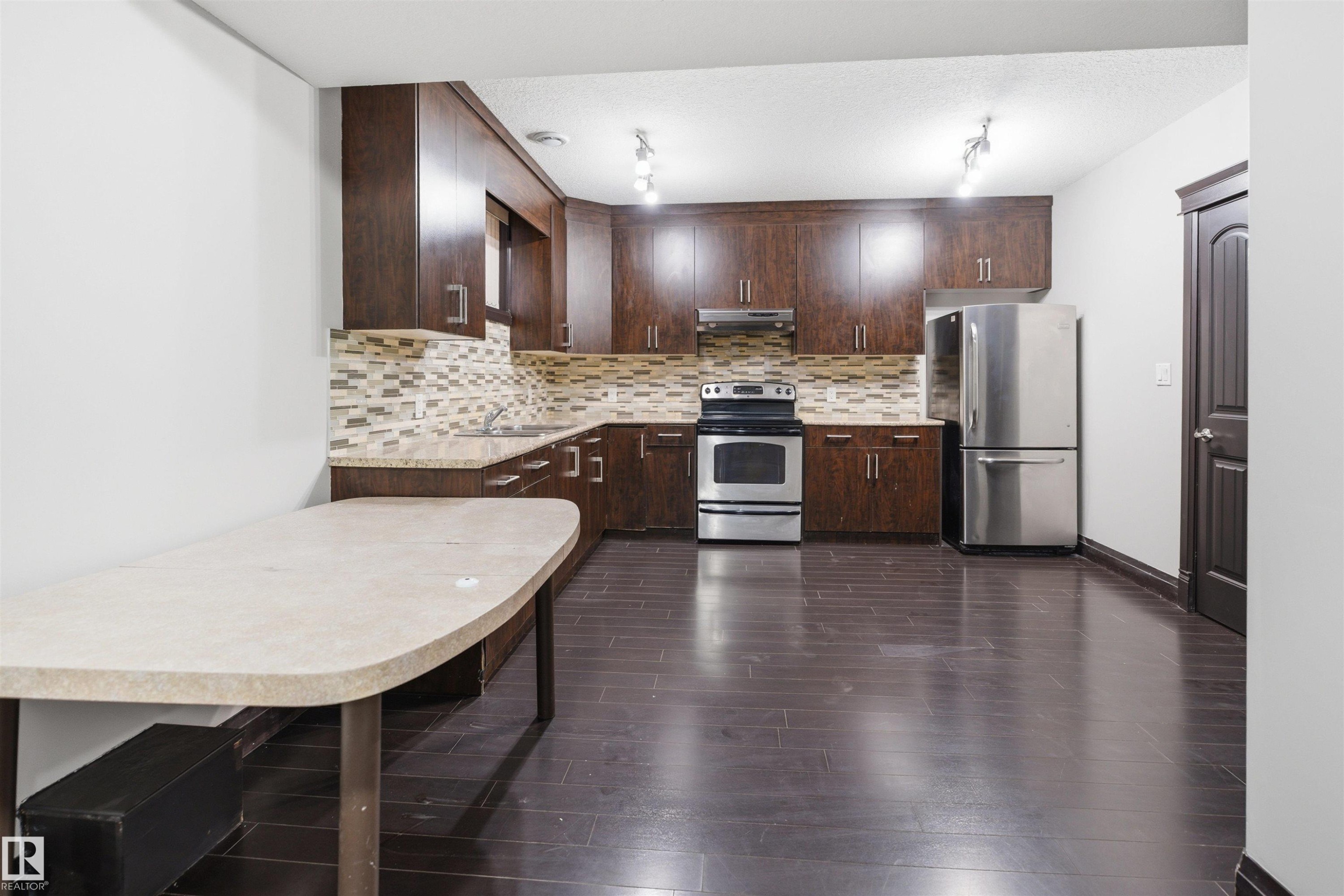 Kitchen featuring dark wood-finish cabinetry, stainless steel appliances, mosaic tile backsplash, and a light-toned countertop - 16807 54 Street, Edmonton, AB - Indoor Photo Showing Kitchen With Stainless Steel Kitchen With Upgraded Kitchen