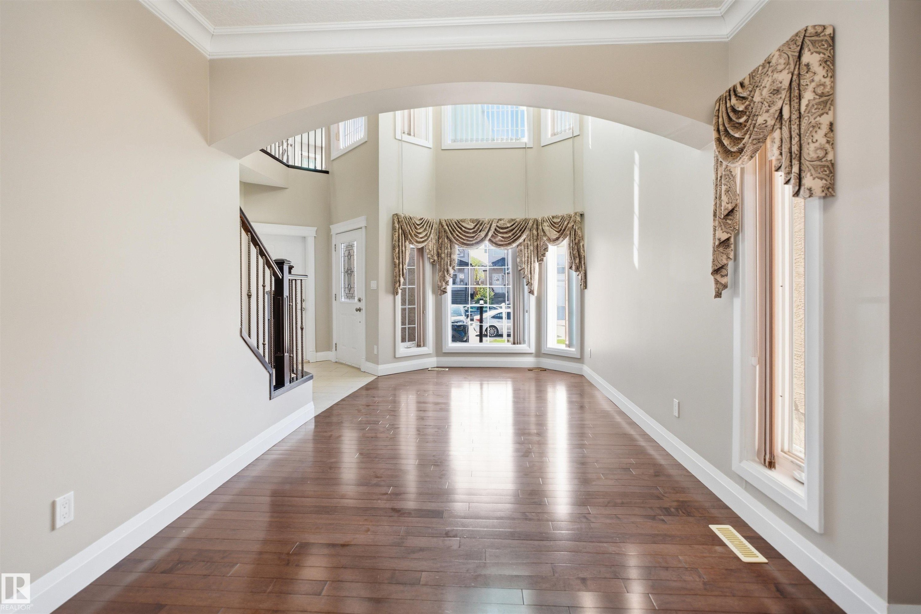 Bright entryway with wood-finish flooring and a grand staircase featuring dark wood newel posts and spindles - 16807 54 Street, Edmonton, AB - Indoor Photo Showing Other Room