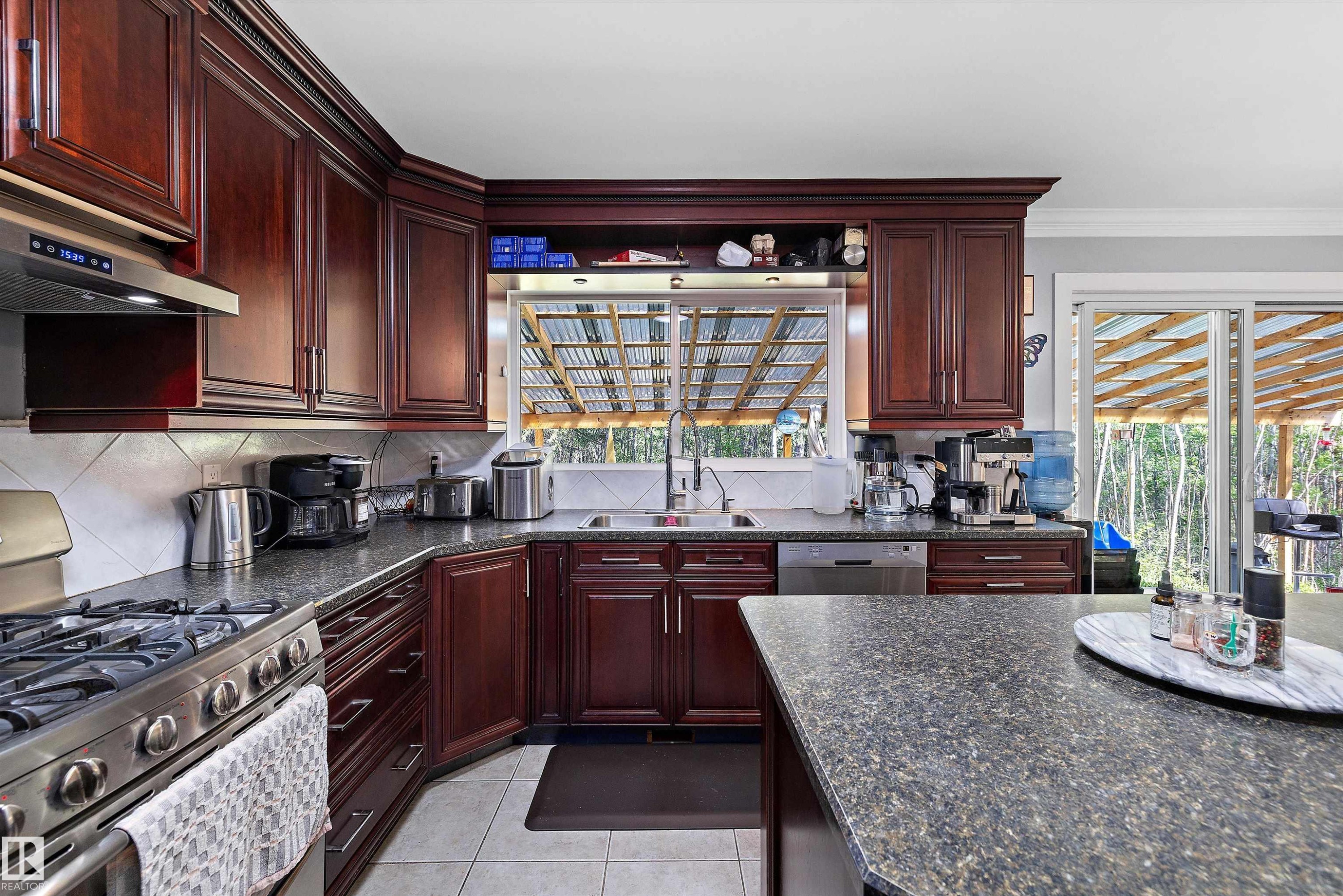 Kitchen featuring dark wood-finish cabinetry, speckled countertops, stainless steel appliances, and a tile backsplash - 53257 Rge Road 211, Rural Strathcona County, AB - Indoor Photo Showing Kitchen With Double Sink