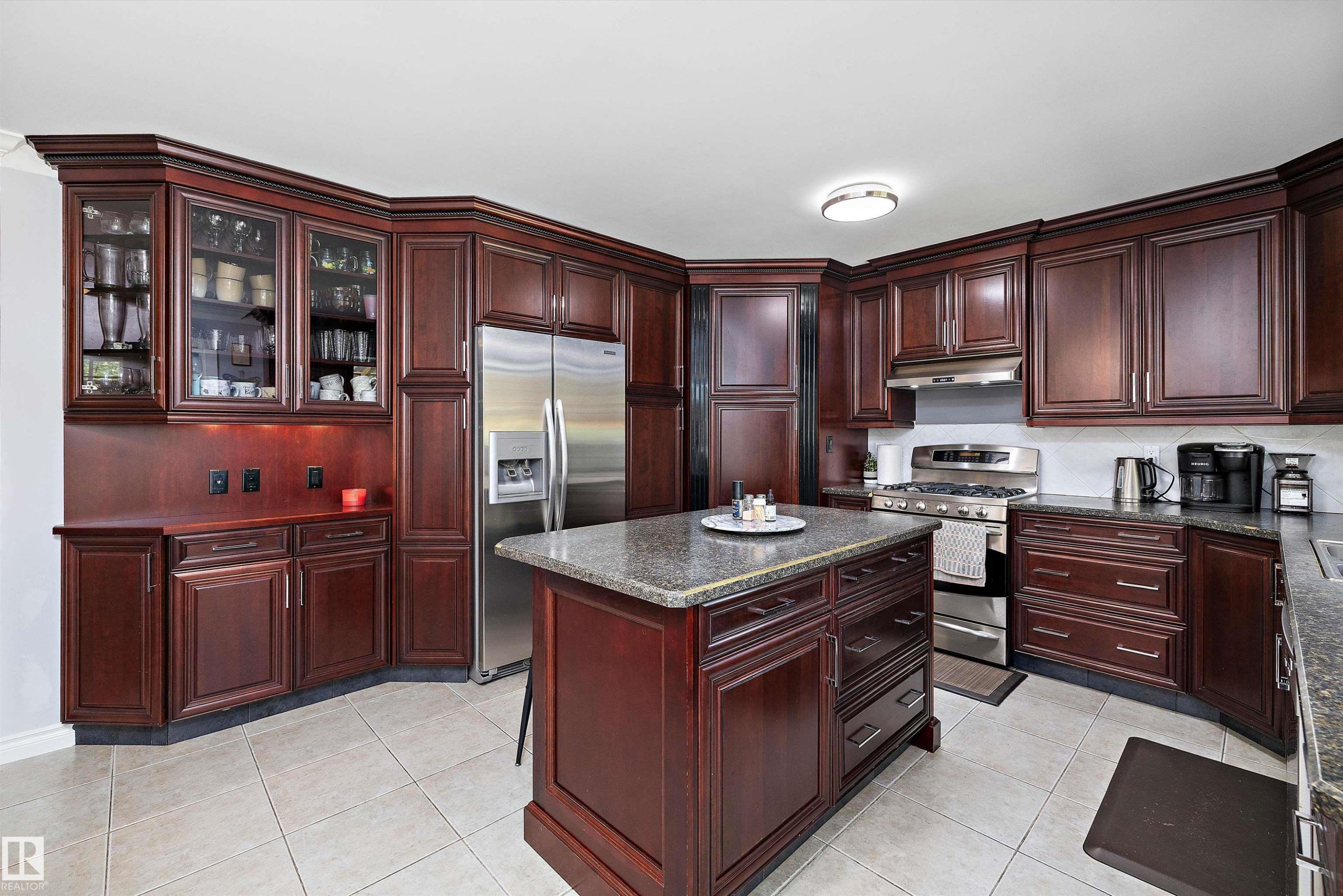 Kitchen featuring dark wood cabinetry, a central island with a granite-style countertop, stainless steel appliances, and light-toned tile flooring - 53257 Rge Road 211, Rural Strathcona County, AB - Indoor Photo Showing Kitchen