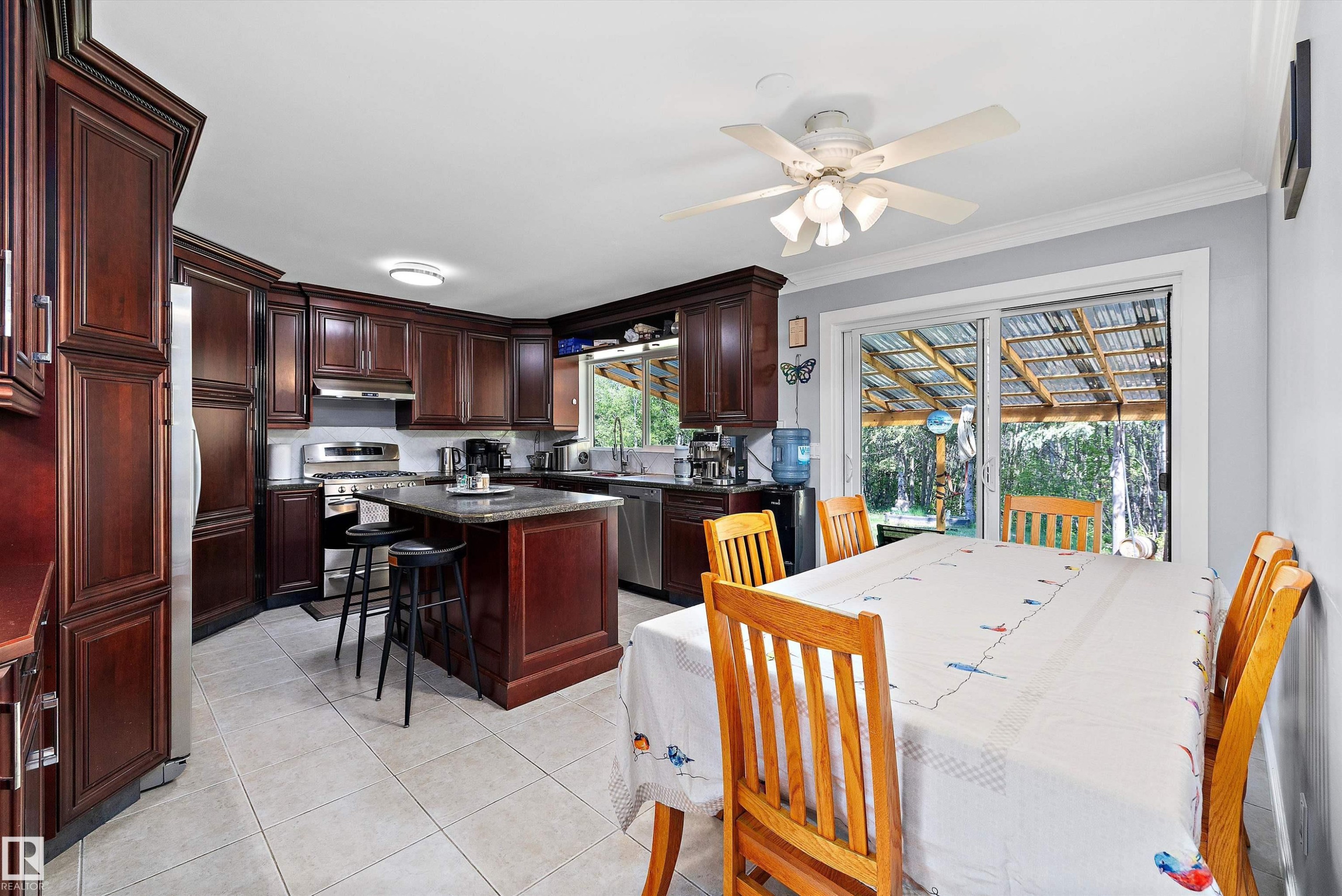 Kitchen and dining area featuring dark wood cabinetry, stainless steel appliances, a center island with bar seating, a ceiling fan, and sliding glass doors - 53257 Rge Road 211, Rural Strathcona County, AB - Indoor Photo Showing Dining Room