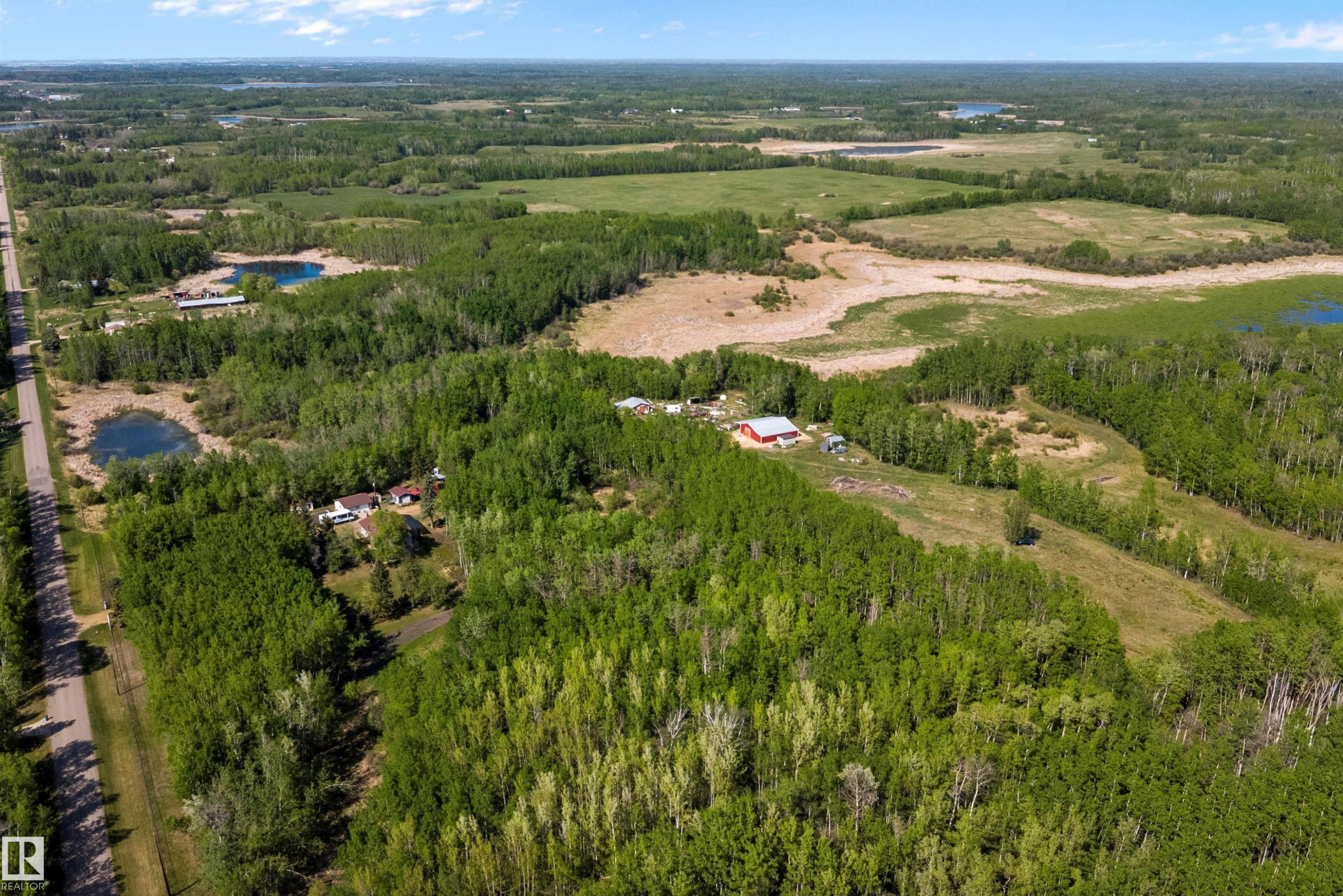 Expansive rural landscape featuring a single-family home and barn structure surrounded by mature trees, open fields, and natural water bodies - 53257 Rge Road 211, Rural Strathcona County, AB - Outdoor With View