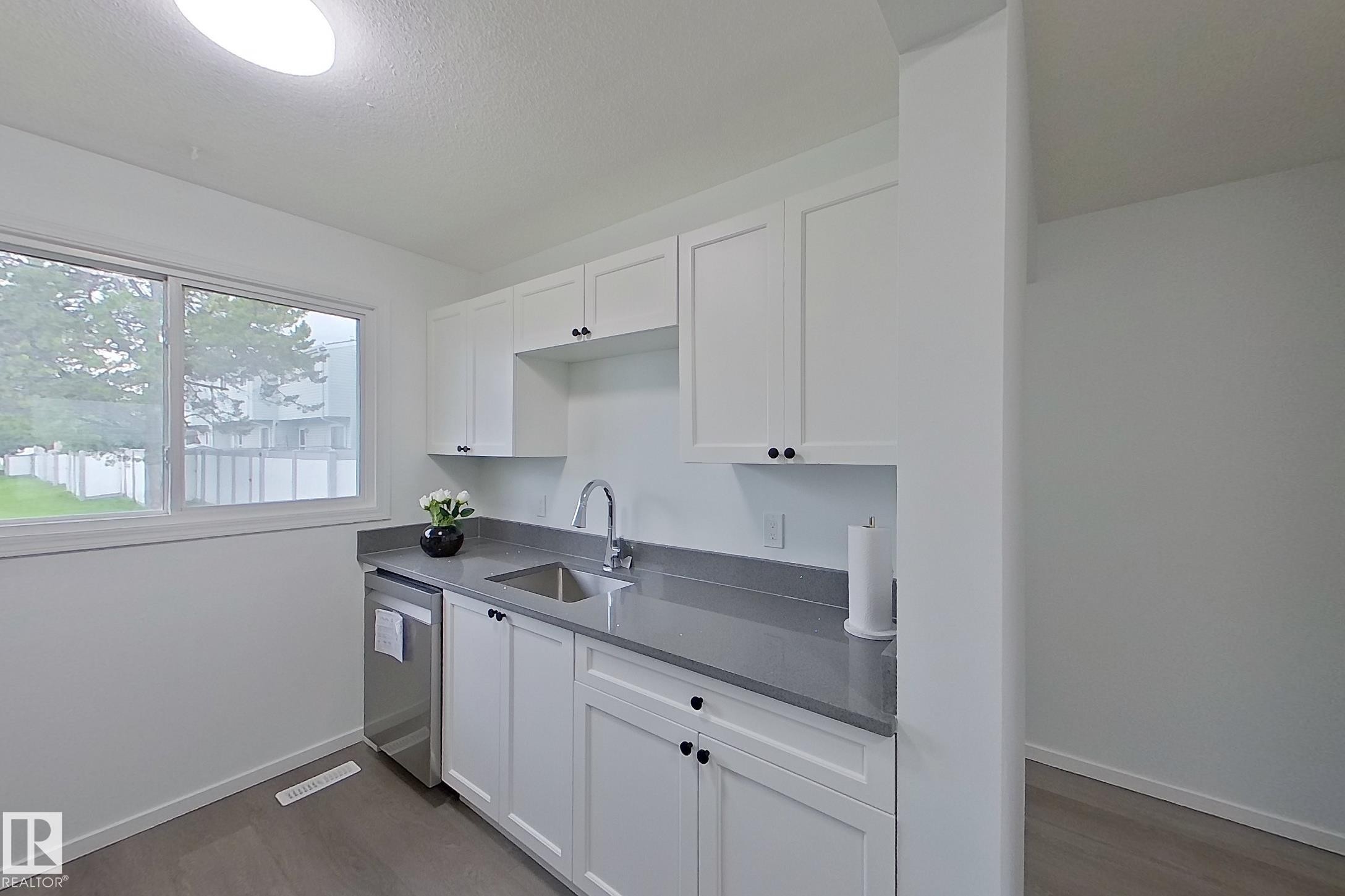 Kitchenette featuring white cabinetry, gray countertops, a stainless steel sink, and a built-in dishwasher - 209 Dickinsfield Court Nw, Edmonton, AB