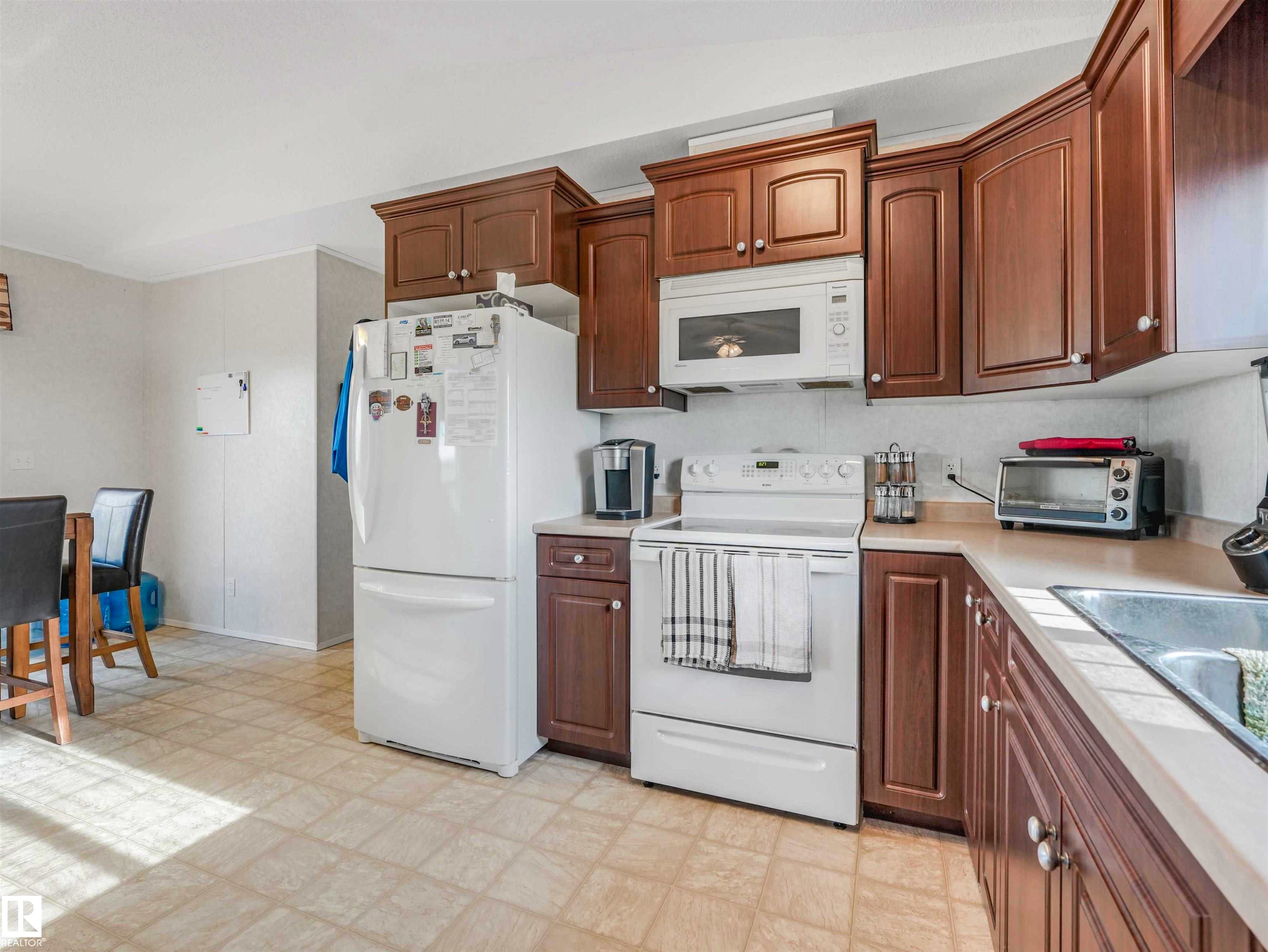 Kitchen featuring wood-finish cabinetry, white appliances including a refrigerator, range, and microwave, and a double basin sink - 57016 Range Road 13, Rural Barrhead County, AB - Indoor Photo Showing Kitchen