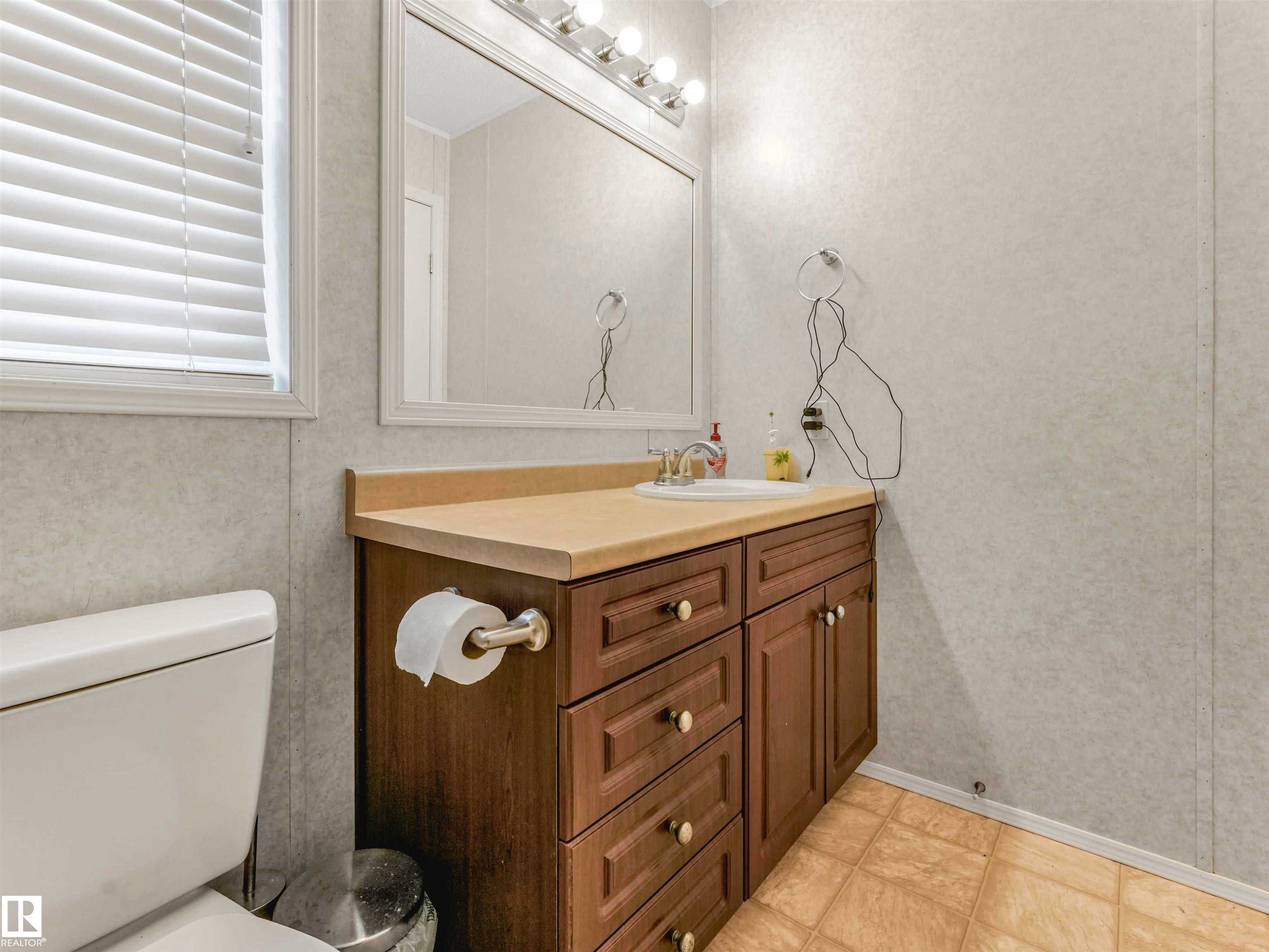 Bathroom featuring a wood-finish vanity with a built-in sink, a neutral countertop, and a large wall-mounted mirror with overhead lighting - 57016 Range Road 13, Rural Barrhead County, AB - Indoor Photo Showing Bathroom