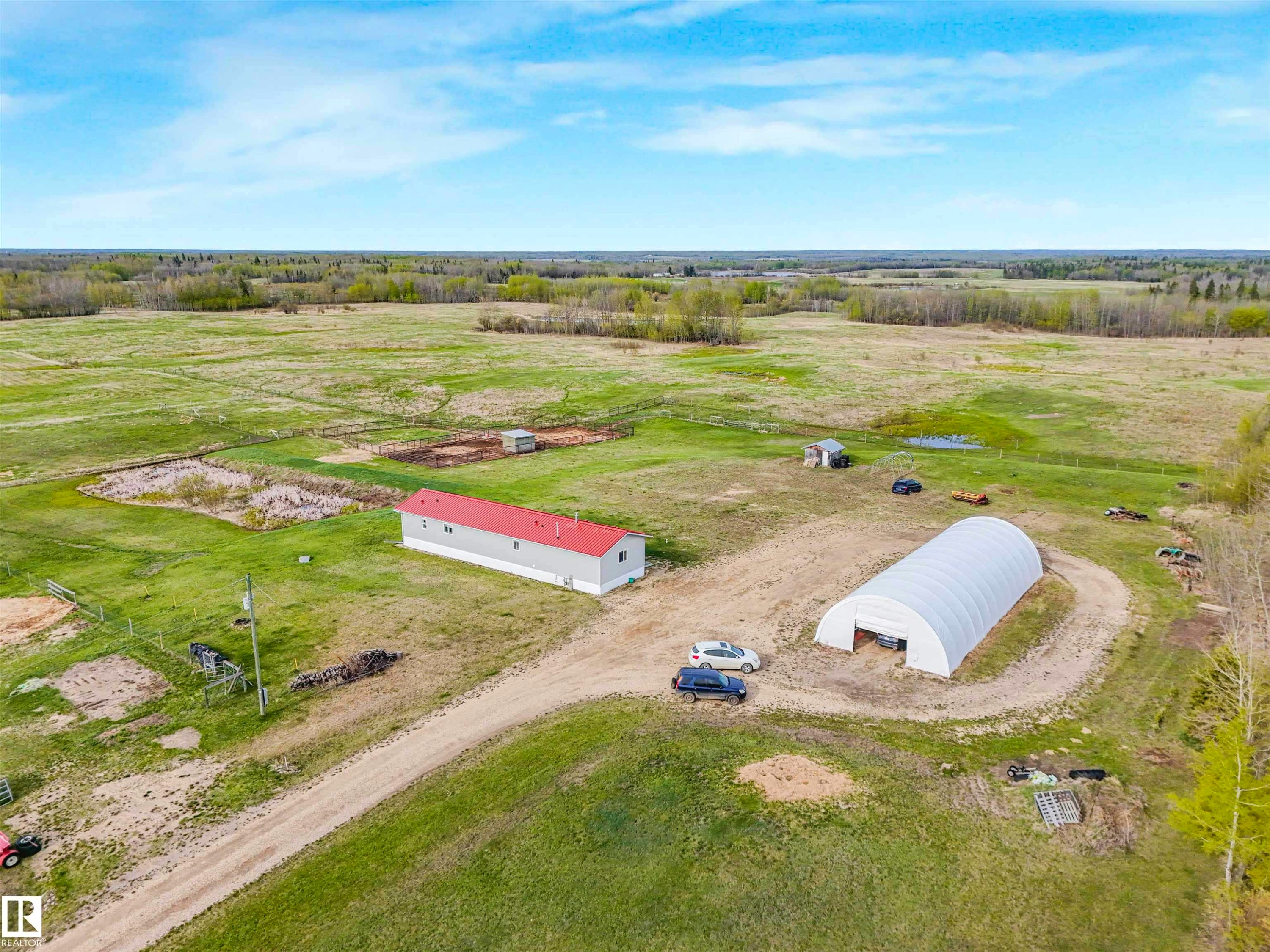 Expansive rural property featuring a primary structure with a red metal roof, a large hoop-style outbuilding, and a dirt driveway - 57016 Range Road 13, Rural Barrhead County, AB - Outdoor With View
