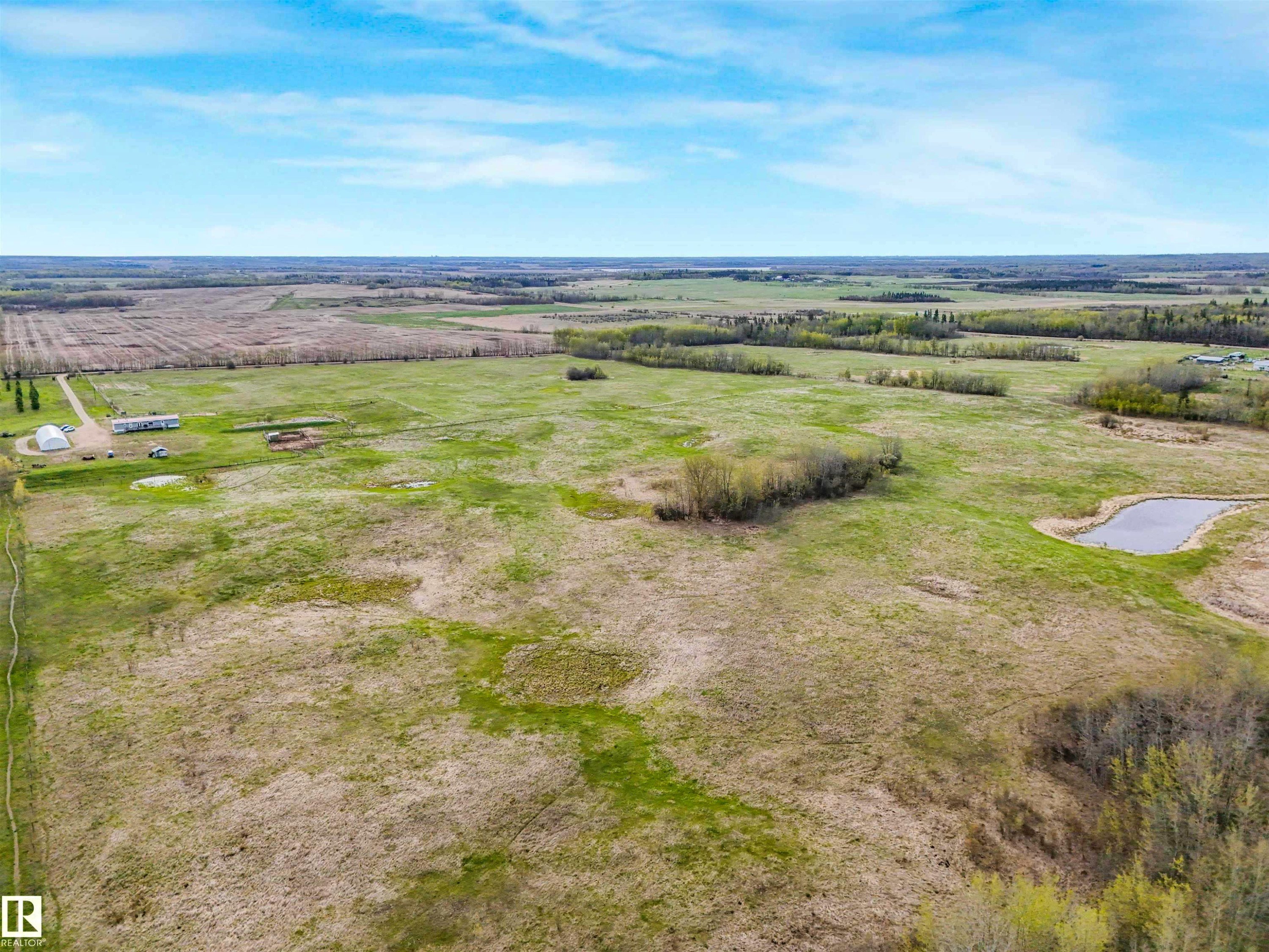 Expansive rural property featuring an established gravel driveway, multiple outbuildings including a hoop house, a natural pond, and cultivated fields - 57016 Range Road 13, Rural Barrhead County, AB - Outdoor With View