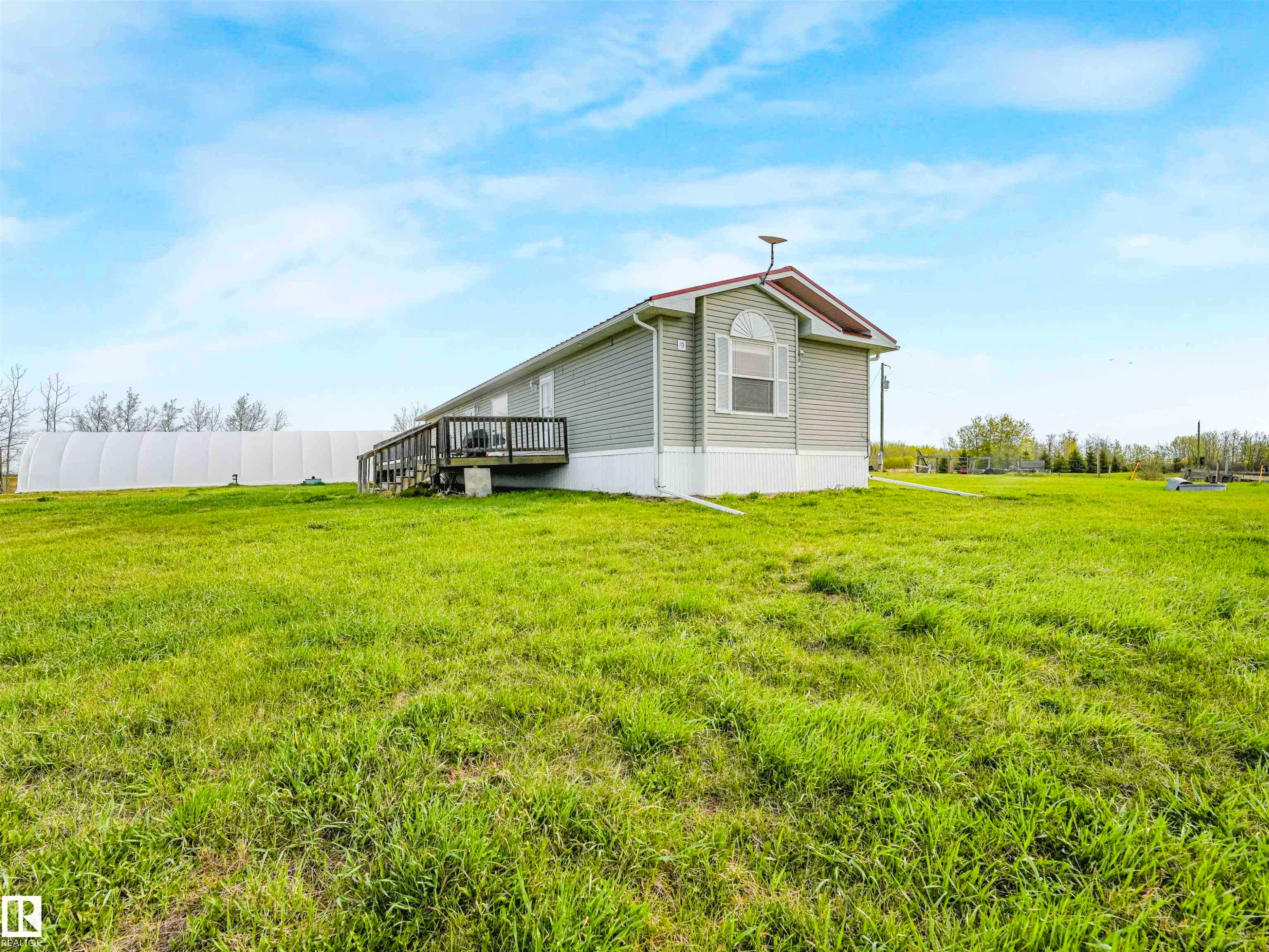 Siding exterior with a gable roofline, featuring an arched window, a wooden deck, and a spacious grassy area - 57016 Range Road 13, Rural Barrhead County, AB - Outdoor