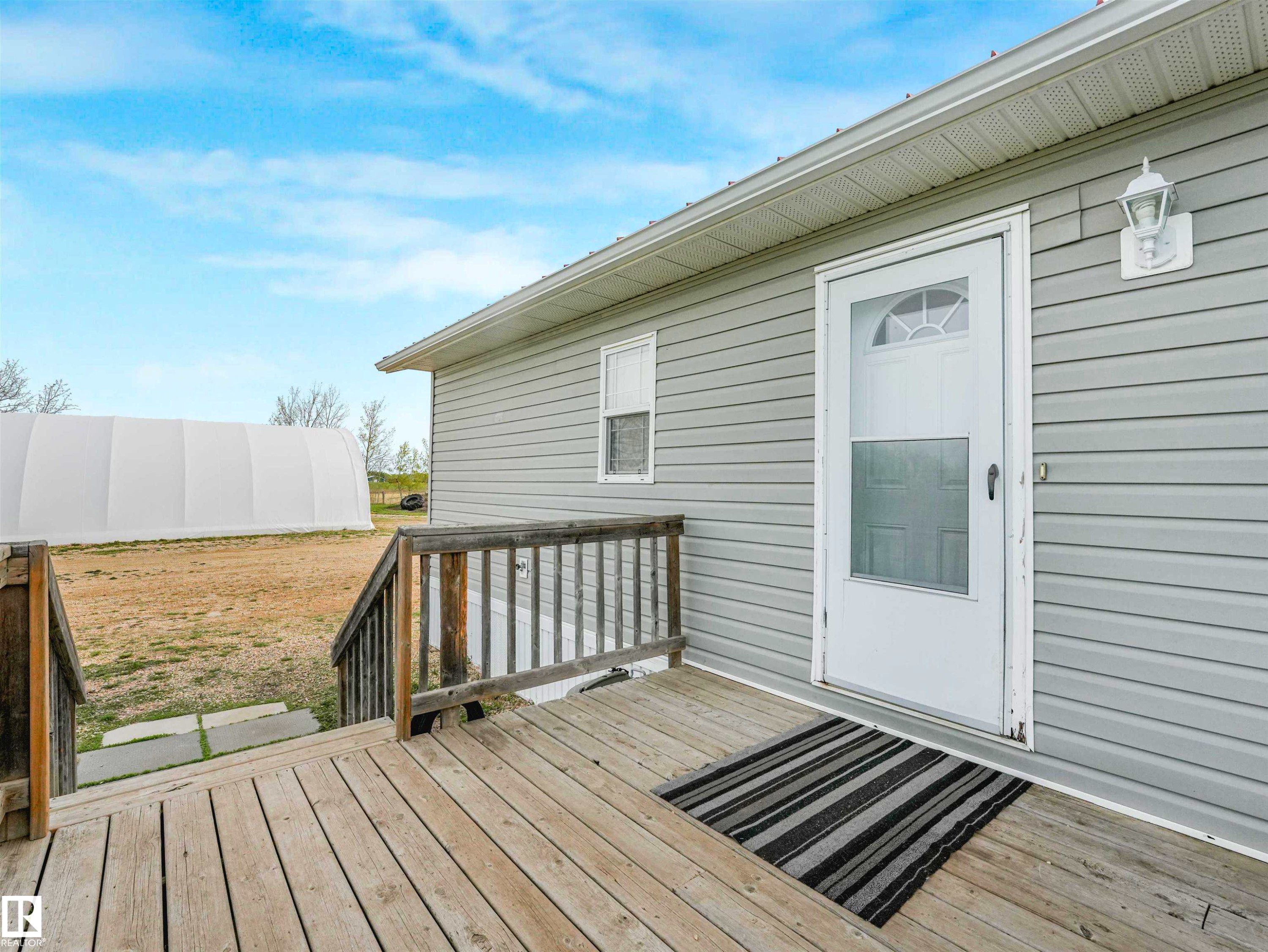 Exterior featuring light grey horizontal siding, a white storm door with a decorative transom, and an attached wood deck with railings - 57016 Range Road 13, Rural Barrhead County, AB - Outdoor With Deck Patio Veranda With Exterior