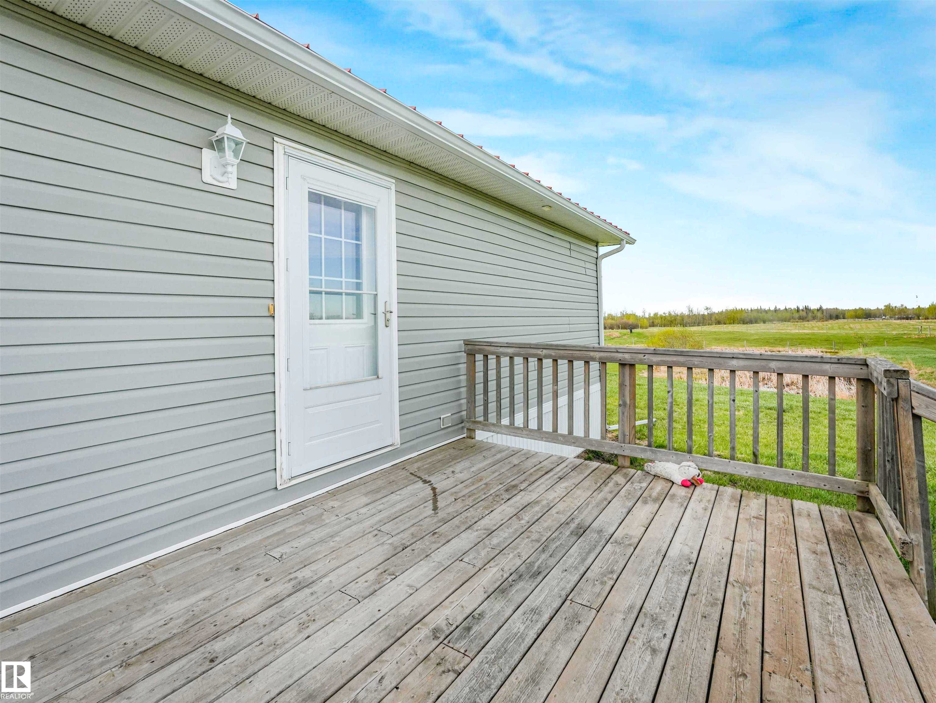 Outdoor wooden deck with railing, featuring a white exterior door with window panes, light gray siding, and an exterior wall lantern - 57016 Range Road 13, Rural Barrhead County, AB - Outdoor With Deck Patio Veranda With Exterior