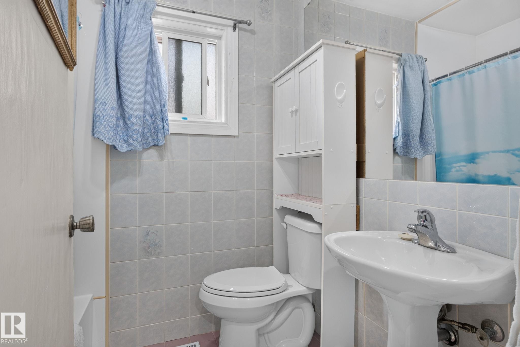 Full bathroom featuring a pedestal sink with chrome faucet, a toilet with an over-the-toilet storage cabinet, and tiled walls - 12703 122 Street Nw, Edmonton, AB