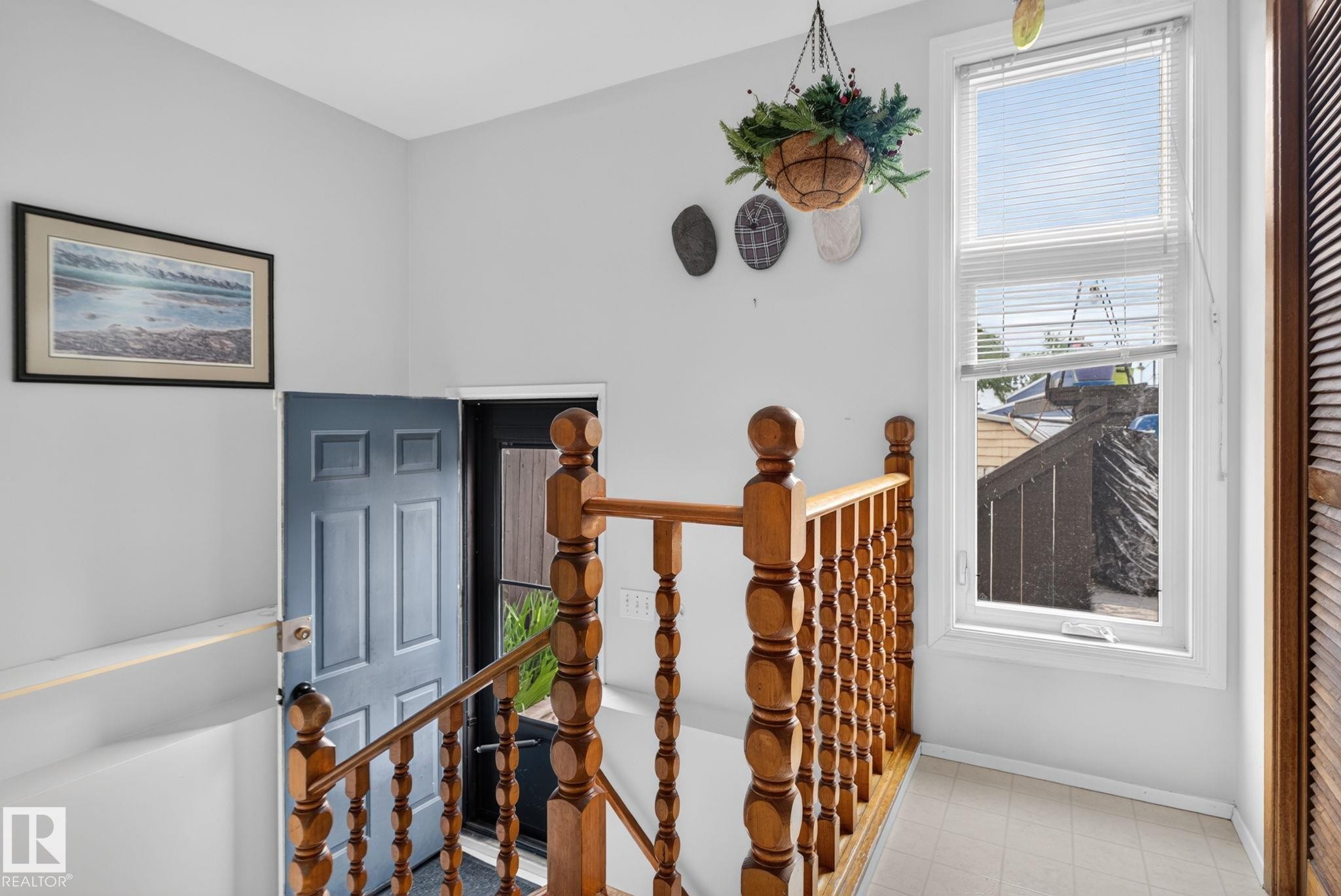 Upper landing featuring wood balustrade and banister, a paneled door, and a single window with horizontal blinds - 12703 122 Street Nw, Edmonton, AB