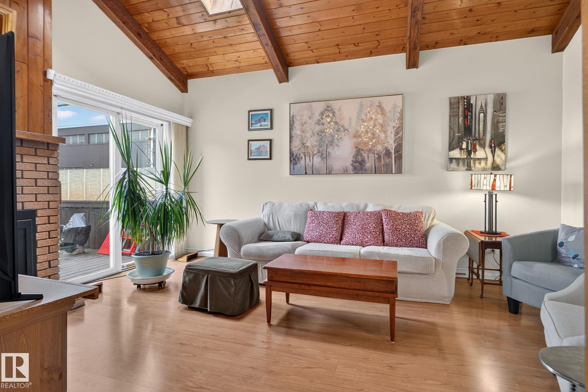 Living area featuring wood-finish flooring, a brick fireplace surround, vaulted wood-beamed ceilings, and a skylight - 12703 122 Street Nw, Edmonton, AB