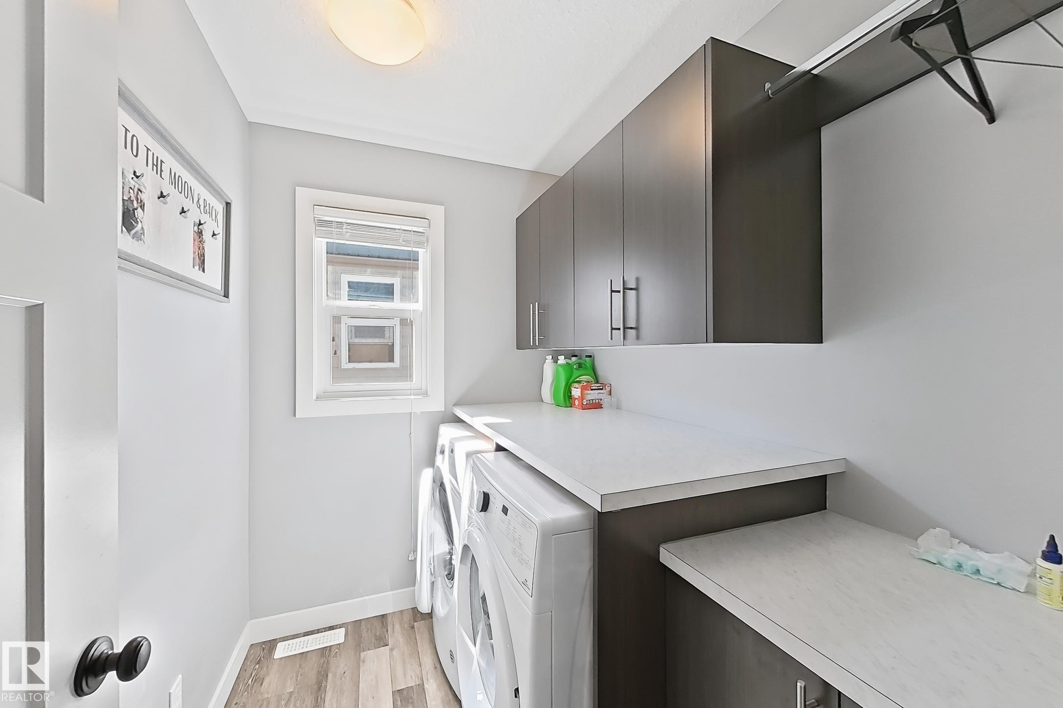 Dedicated laundry area featuring wood-finish flooring, gray walls, and a single window with blinds - 187 Radcliffe Wynd, Fort Saskatchewan, AB - Indoor Photo Showing Laundry Room