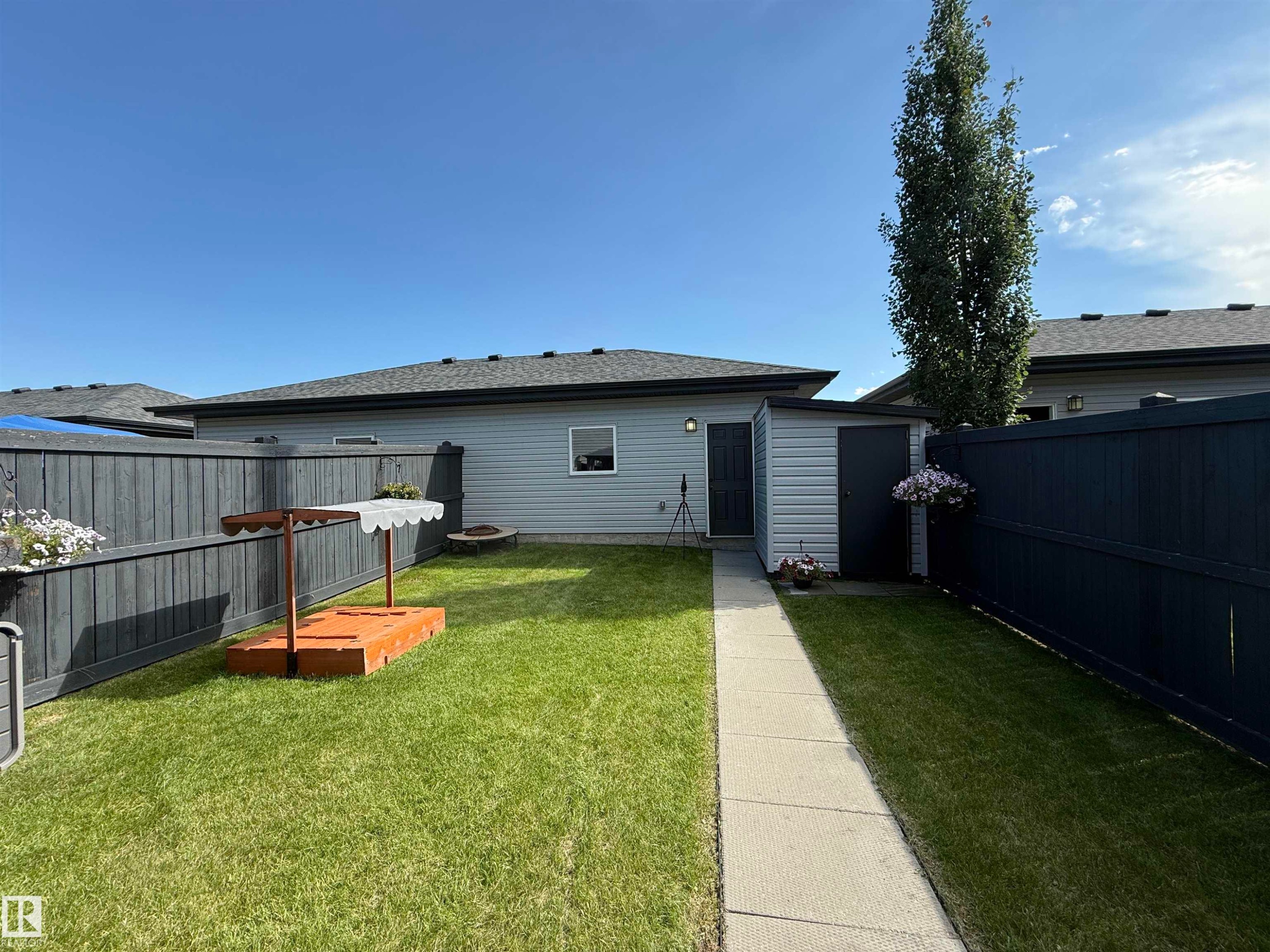 Expansive backyard featuring a manicured lawn, full fencing, a concrete pathway, a storage shed, and a mature tree - 187 Radcliffe Wynd, Fort Saskatchewan, AB - Outdoor