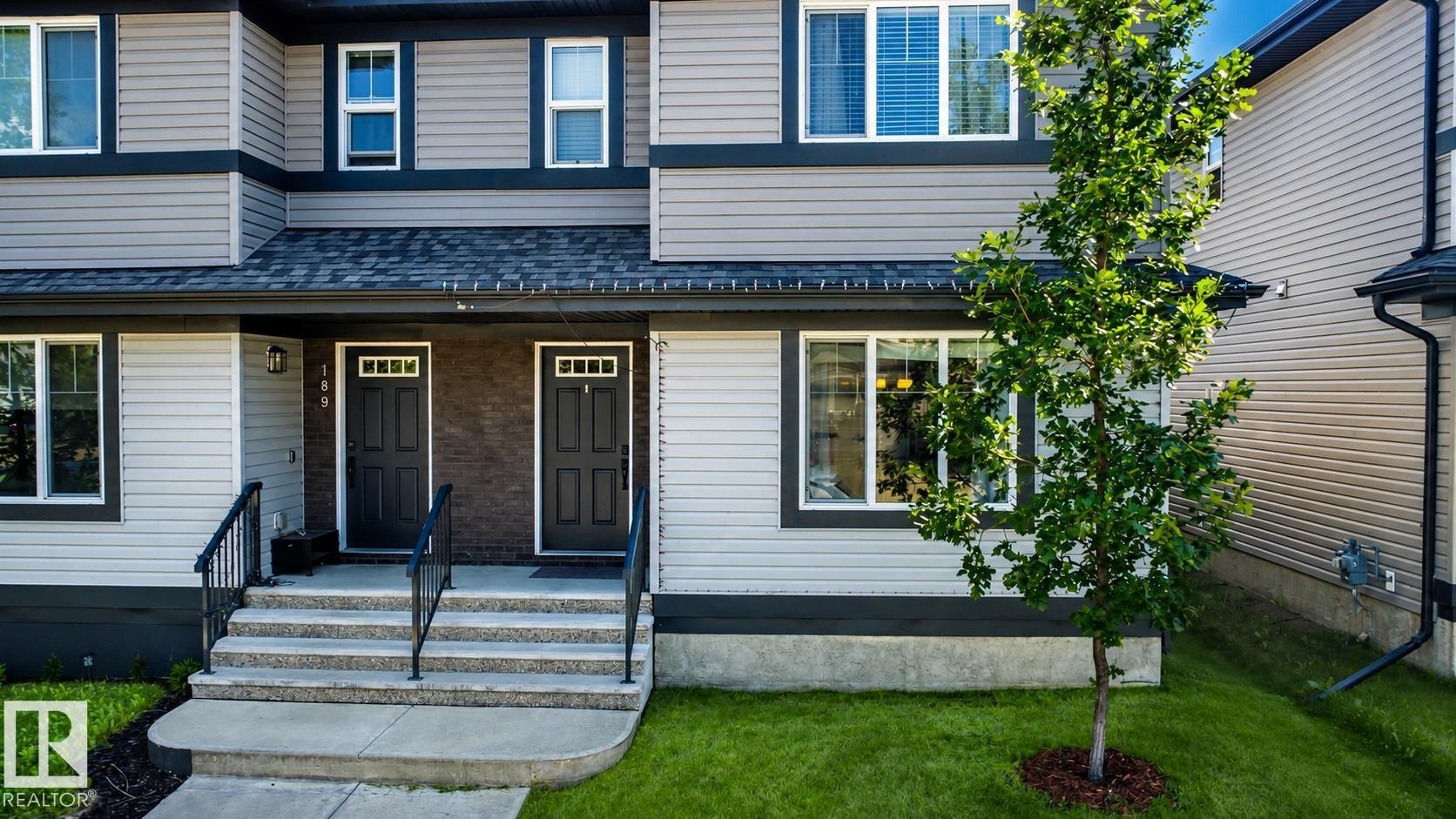 Duplex exterior featuring light gray horizontal siding, dark trim, and a dark asphalt shingle roof - 187 Radcliffe Wynd, Fort Saskatchewan, AB - Outdoor