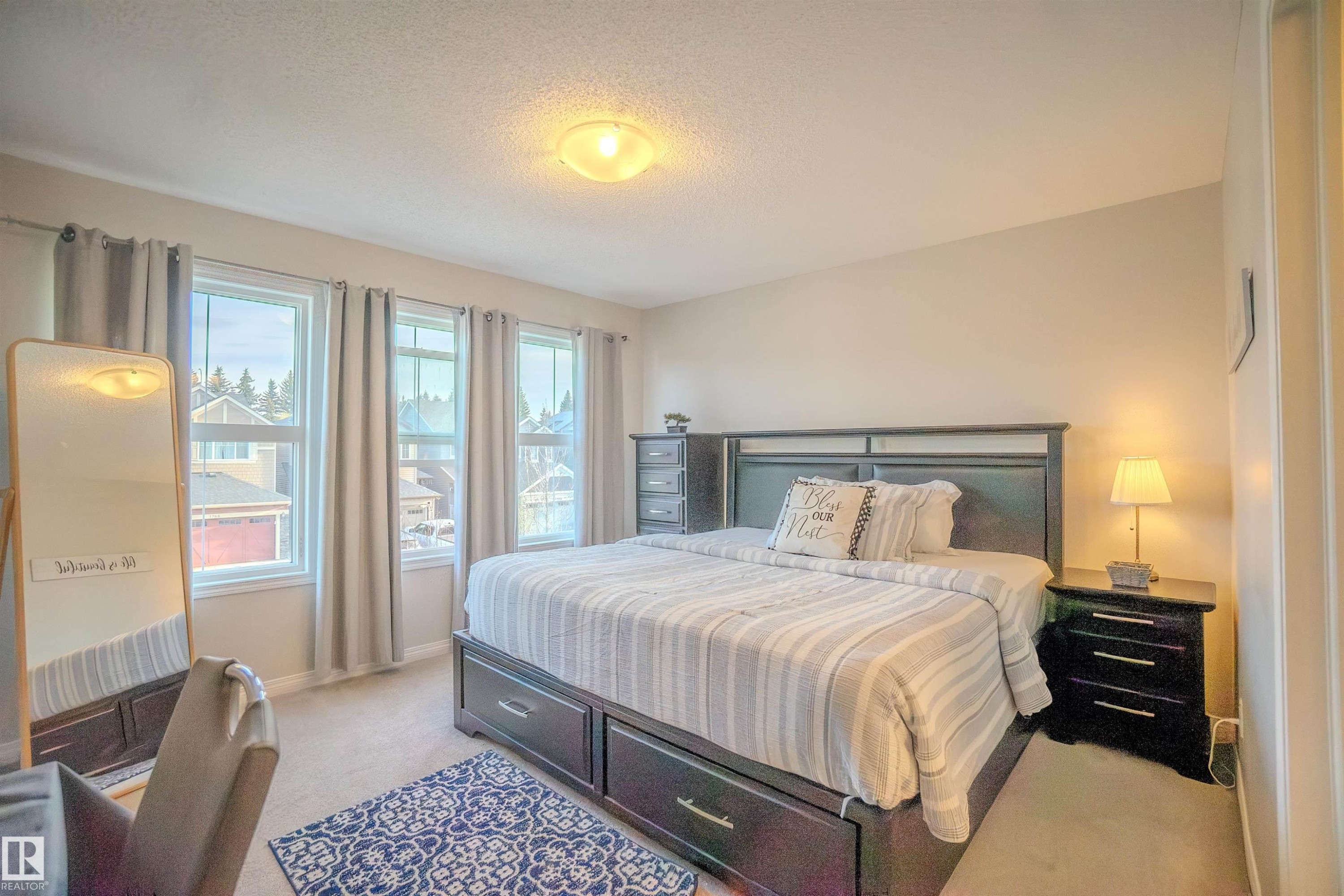 Carpeted room featuring a ceiling-mounted light fixture, three vertical windows with curtains, and neutral wall paint - 1766 Dumont Crescent Sw, Edmonton, AB - Indoor Photo Showing Bedroom