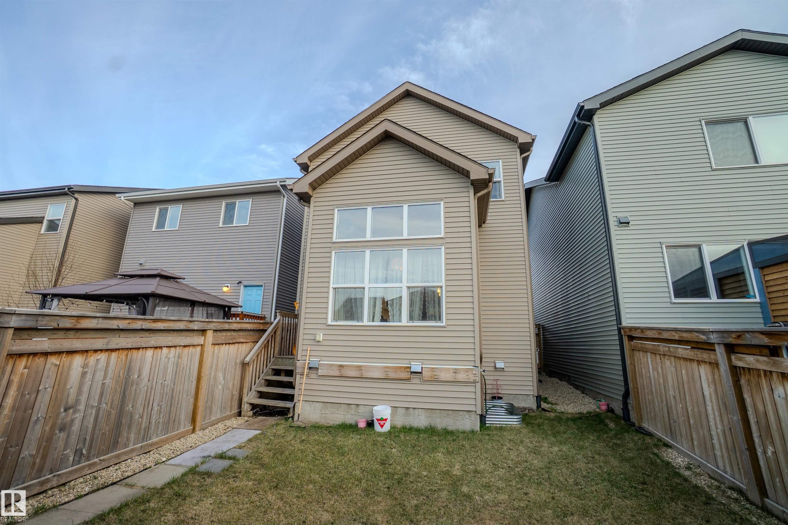 Rear exterior featuring neutral-toned siding, a multi-pane window wall, and a wood staircase leading to an upper entry - 1766 Dumont Crescent Sw, Edmonton, AB - Outdoor With Exterior
