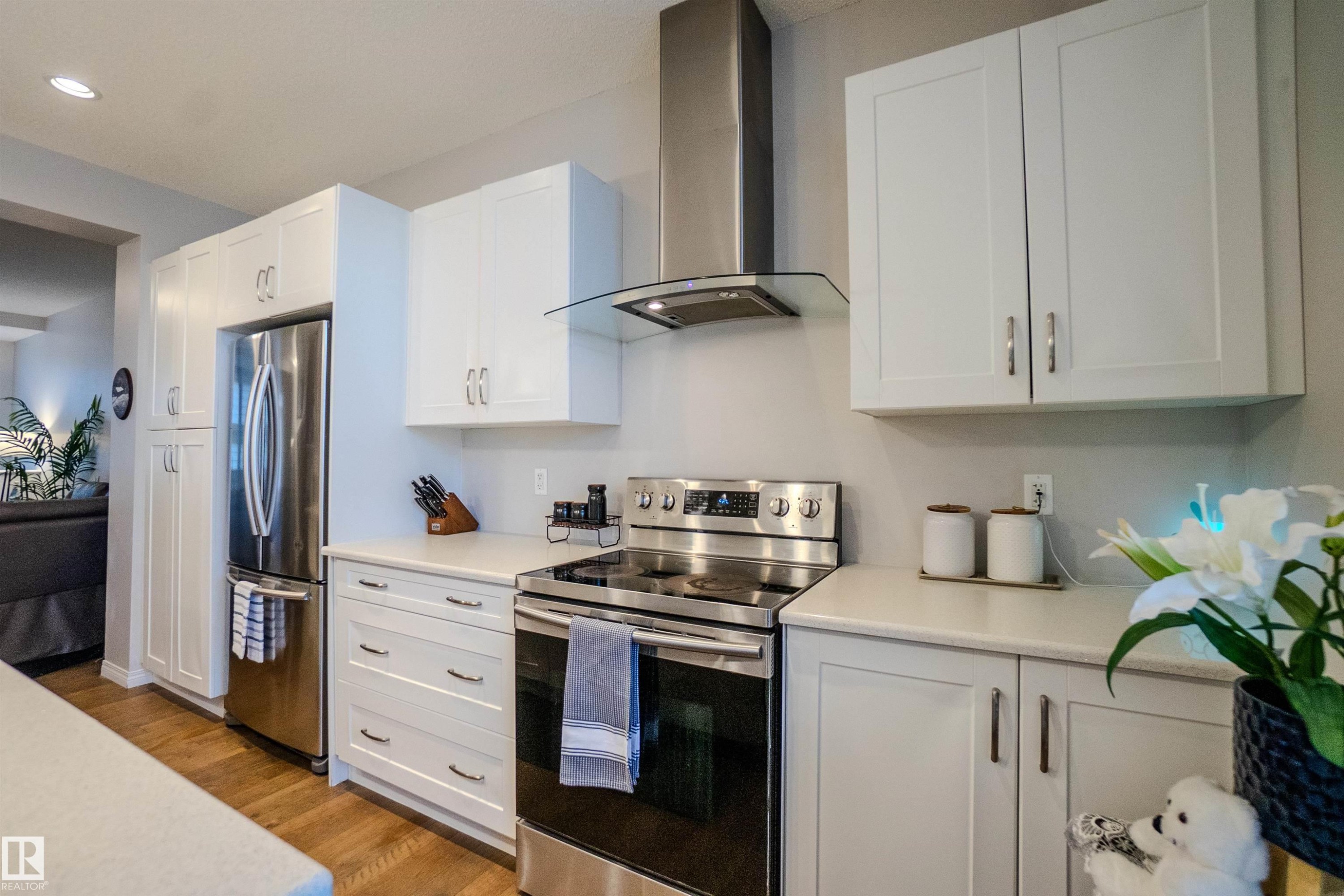 Modern kitchen featuring white cabinetry, stainless steel appliances, a stainless steel range hood, light-toned countertops, and wood-finish flooring - 1766 Dumont Crescent Sw, Edmonton, AB - Indoor Photo Showing Kitchen