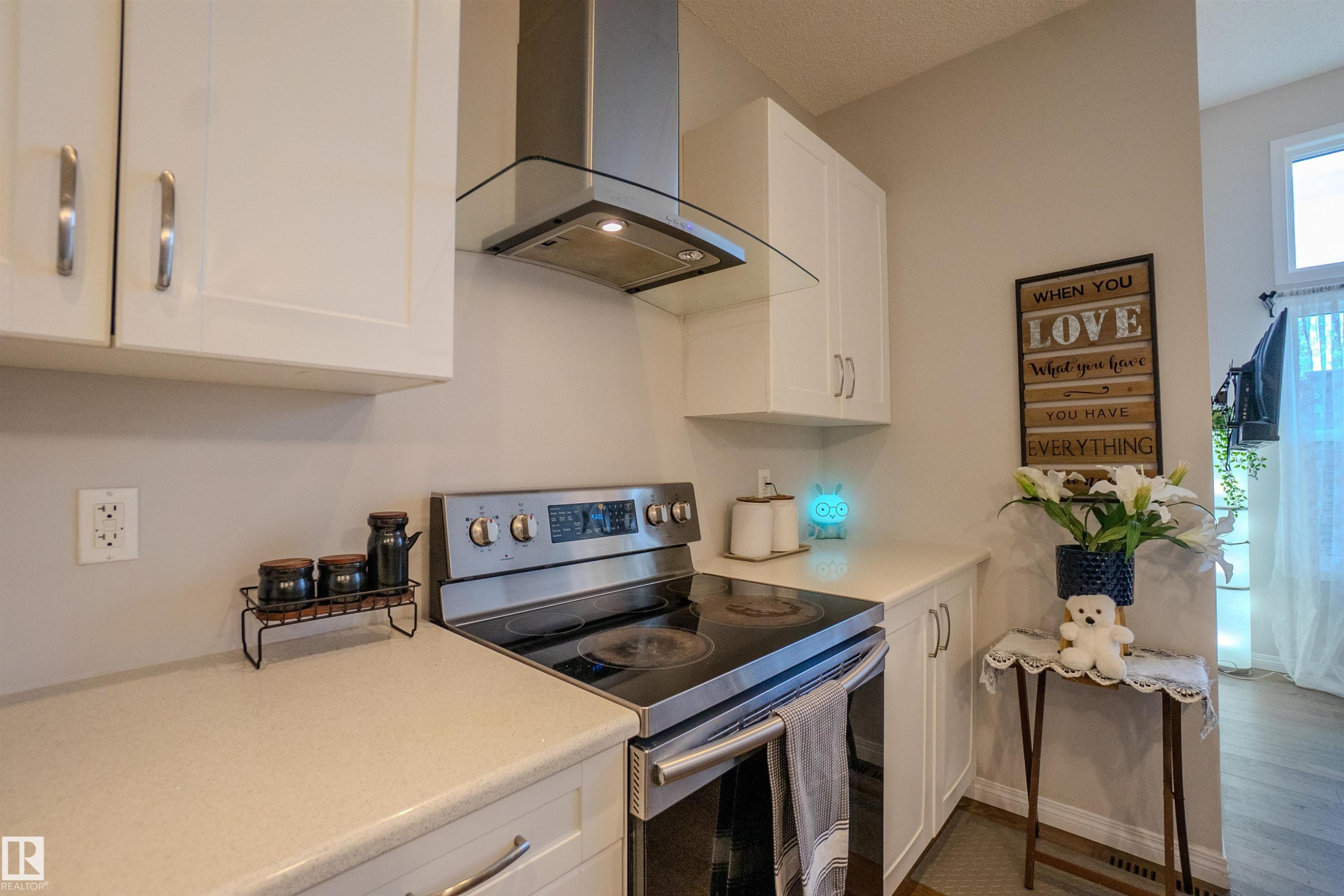 Modern kitchen featuring white cabinetry, light-toned countertops, a stainless steel electric range, and a coordinating stainless steel range hood with glass canopy - 1766 Dumont Crescent Sw, Edmonton, AB - Indoor Photo Showing Kitchen