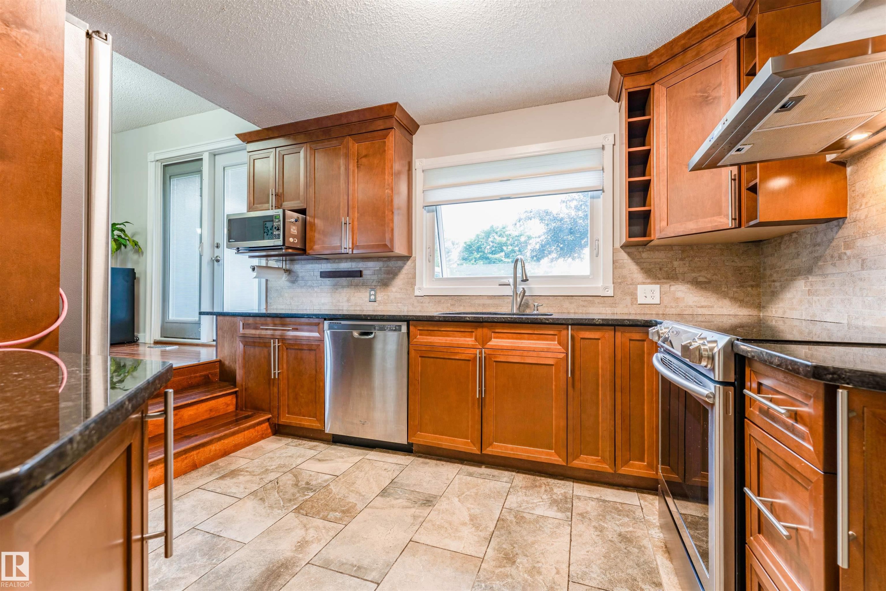 Spacious kitchen featuring warm wood cabinetry, dark countertops, a tile backsplash, and stainless steel appliances - 5212 142 Street Nw, Edmonton, AB