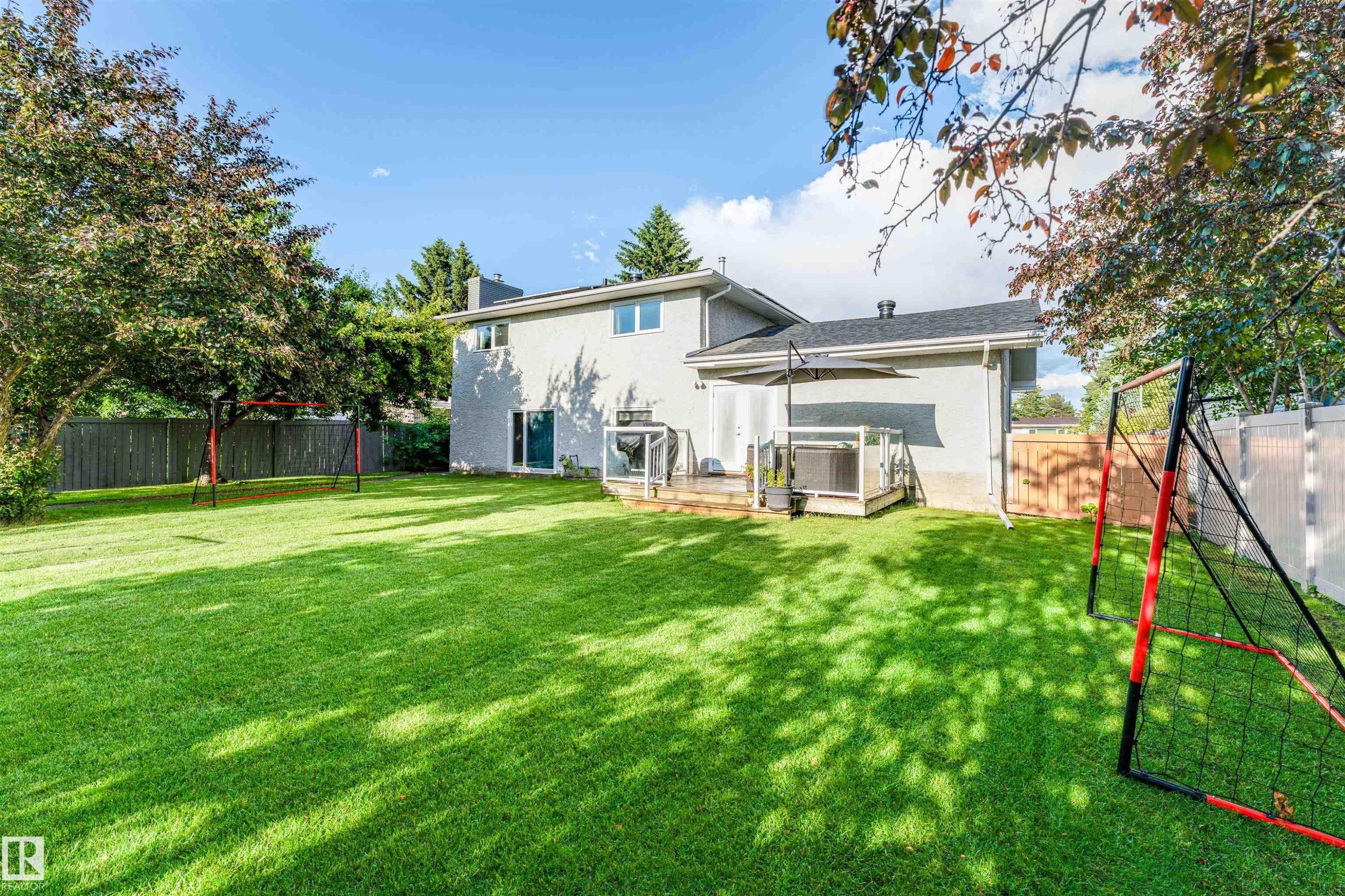 Expansive grassy yard featuring perimeter fencing, mature trees, and a wooden deck with glass railings - 5212 142 Street Nw, Edmonton, AB