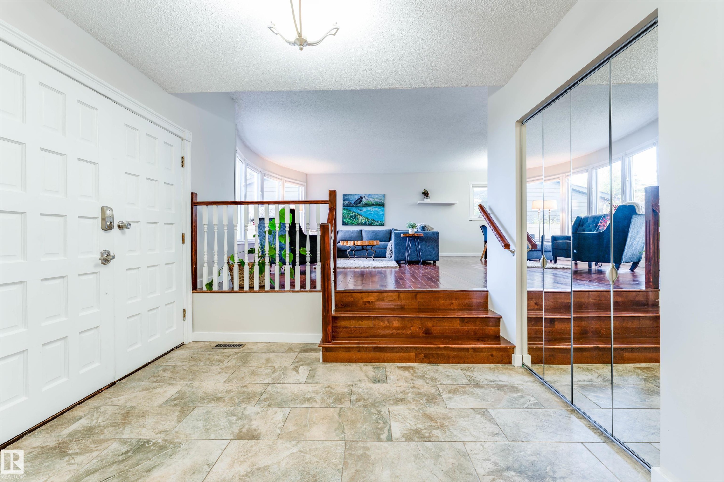 Entry foyer featuring large format tile flooring, a paneled entry door, a mirrored closet, and wood stairs with a white spindle railing - 5212 142 Street Nw, Edmonton, AB