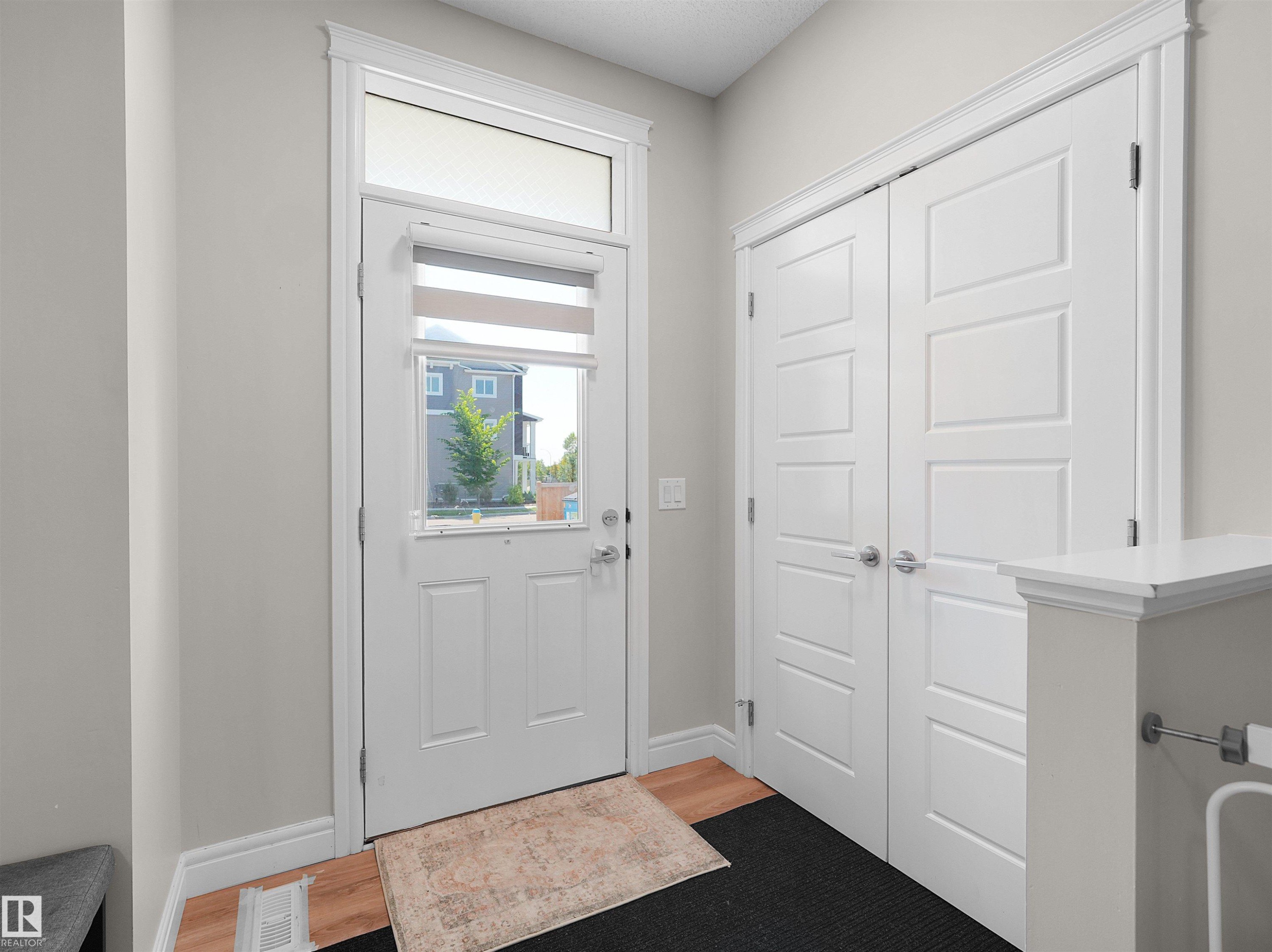Entryway featuring a white paneled door with a transom window, wood-finish flooring, light gray walls, and a built-in double-door storage closet - #30 4137 76 St Nw, Edmonton, AB