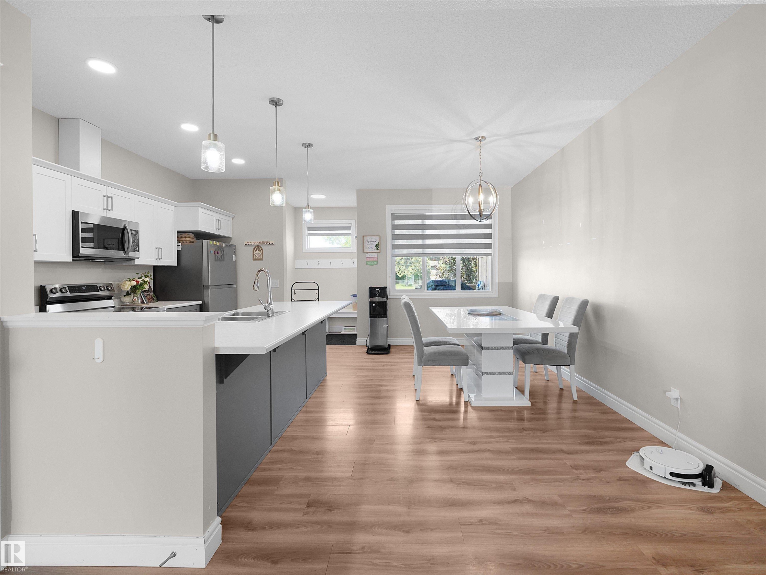 Open-concept kitchen and dining area featuring wood-finish flooring, white cabinetry, and stainless steel appliances - #30 4137 76 St Nw, Edmonton, AB